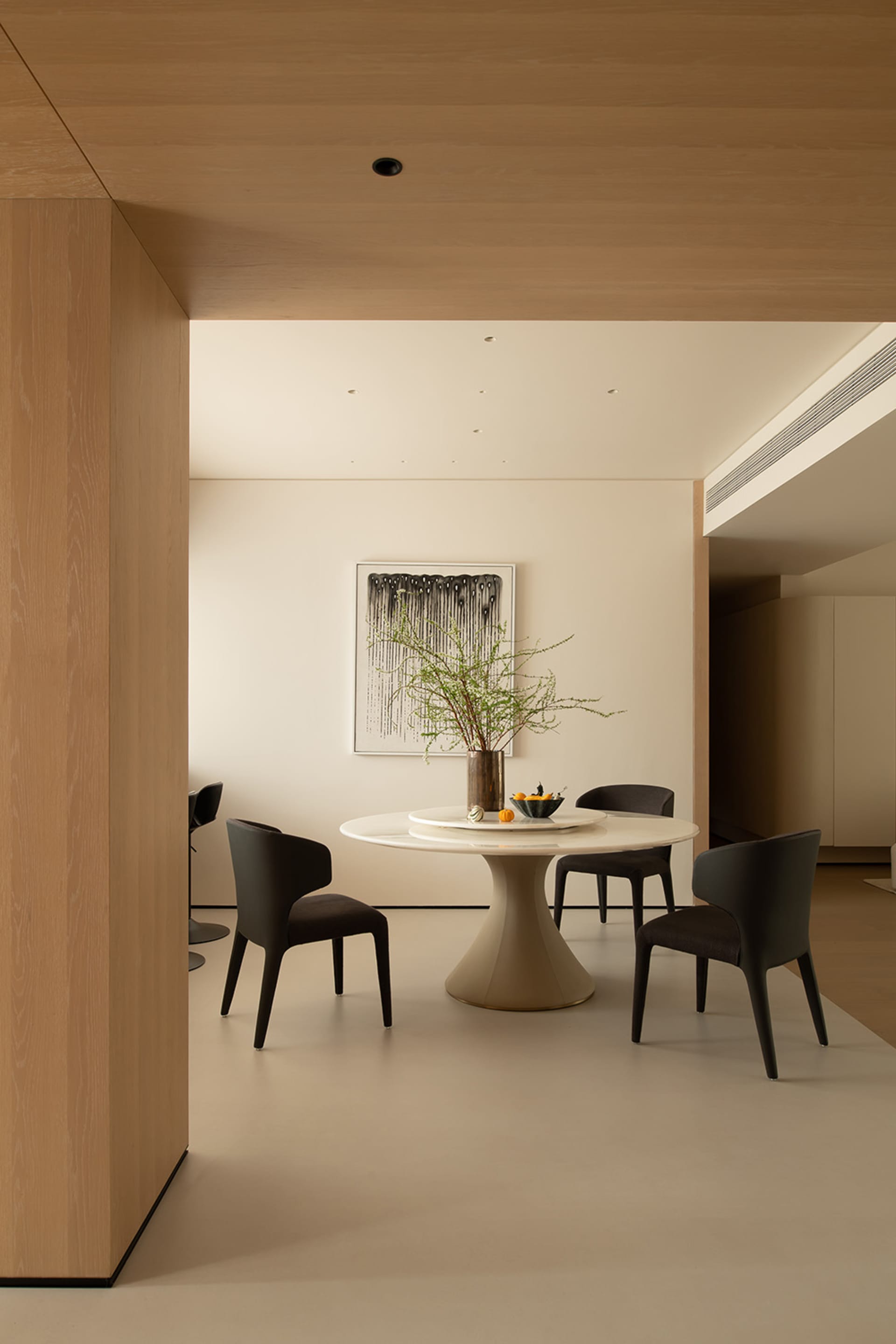 Modern living room with a large white table surrounded by black chairs, a potted plant, and a couch, featuring clean lines and minimalistic design elements