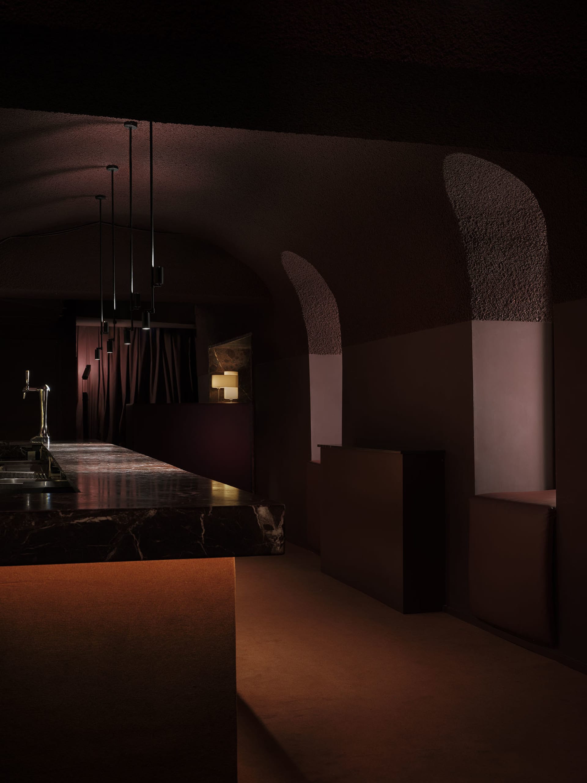 Dark modern bar with a marble counter, brown color scheme, and dim lighting