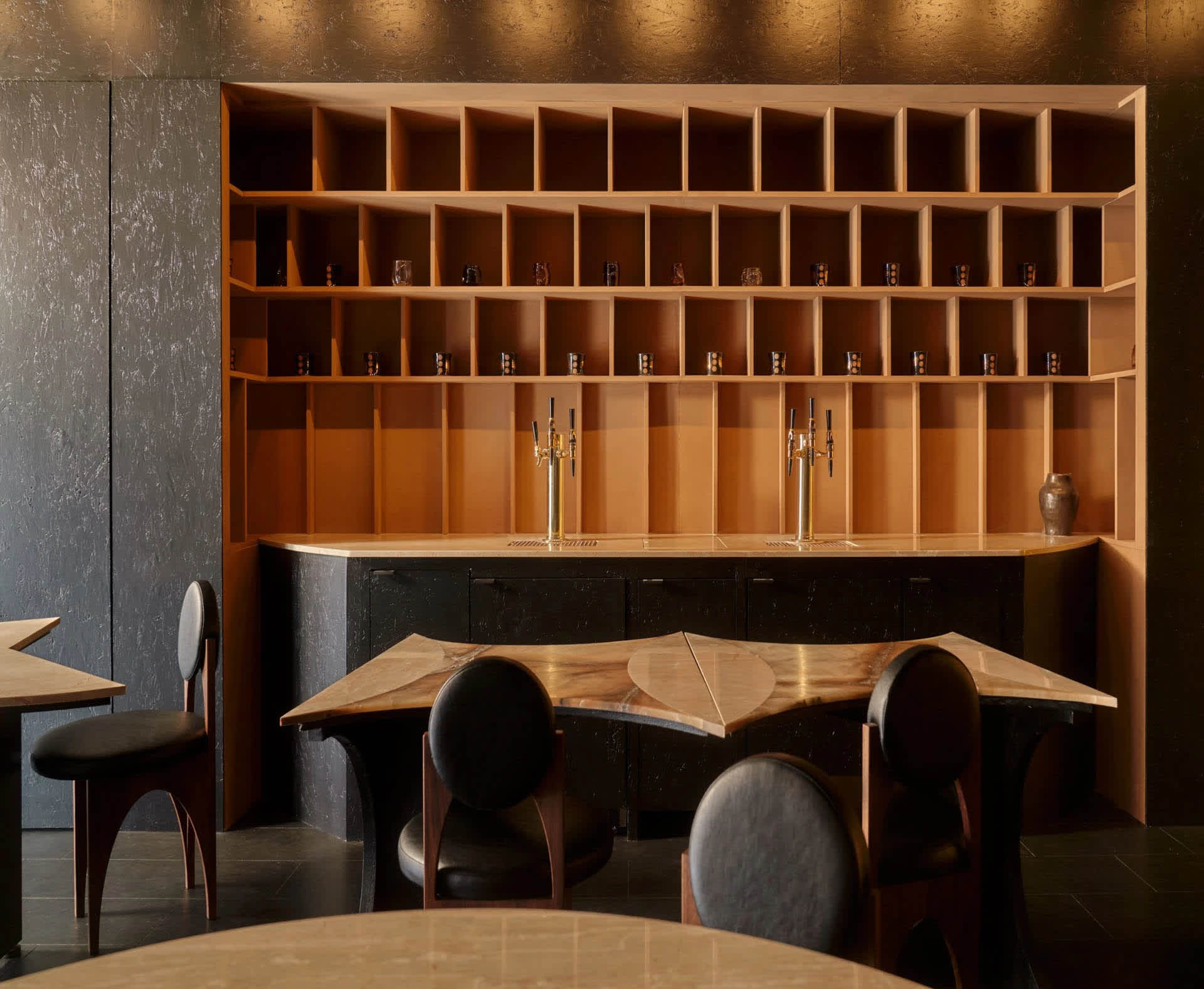 A bar area with a wooden counter, multiple chairs, and a dining table, featuring a well-equipped bar with bottles and wine glasses, creating an inviting and comfortable atmosphere