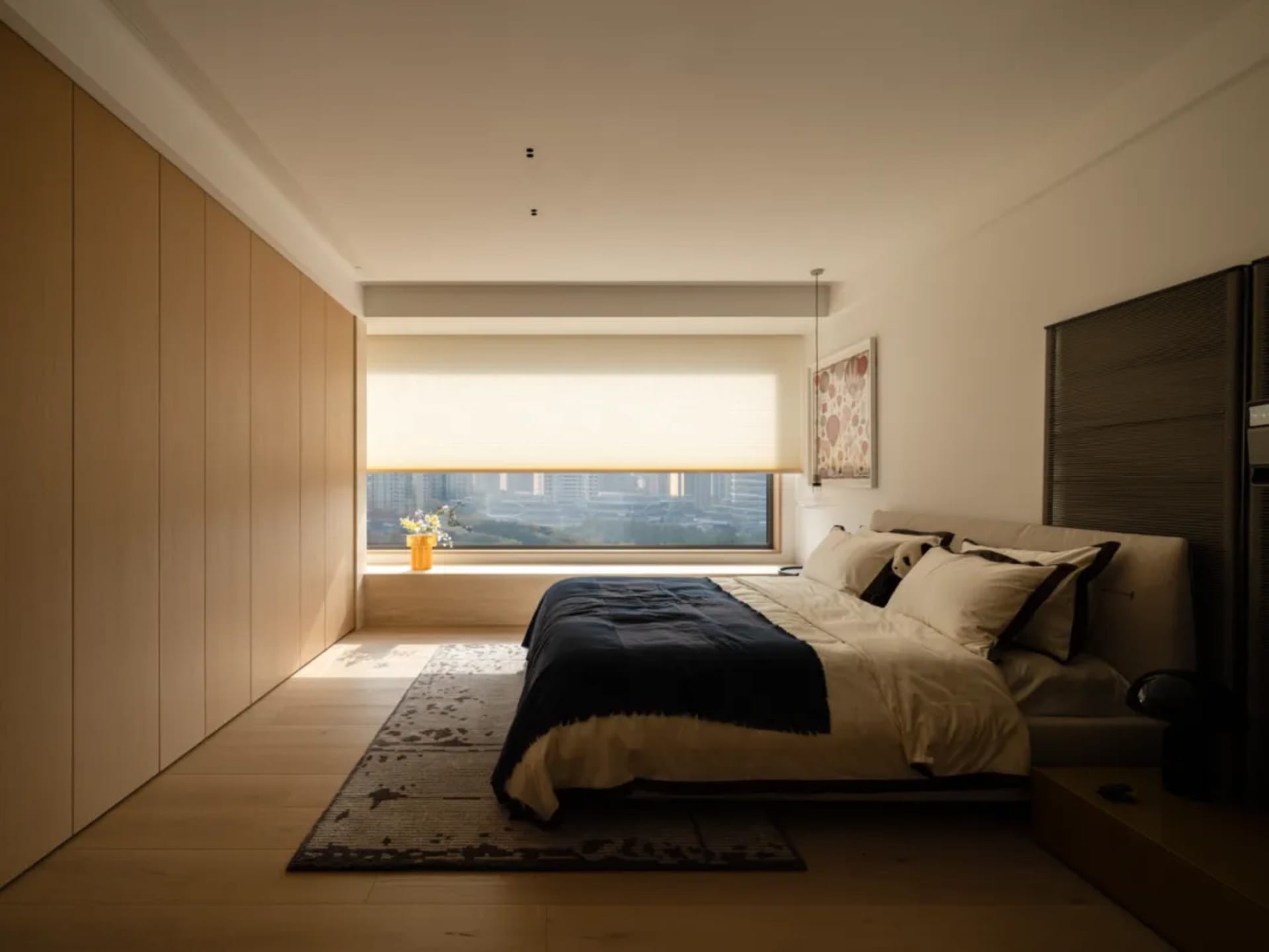 A well-lit bedroom with a bed, chair, and window, featuring wood and glass materials in a neutral color palette