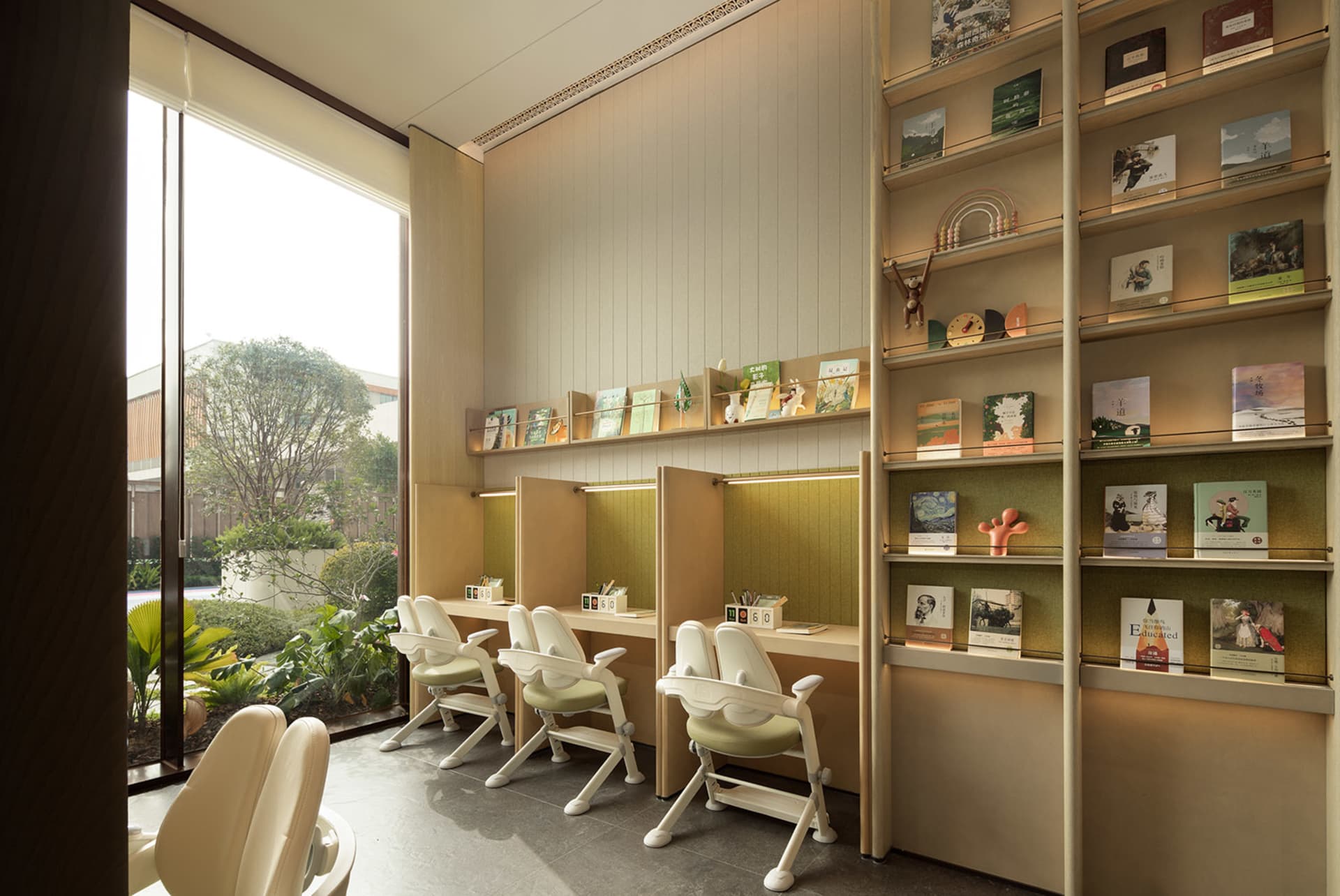 A cozy study area with a wooden floor, white walls, and a large window, featuring comfortable seating and book-filled tables, with soft and warm lighting