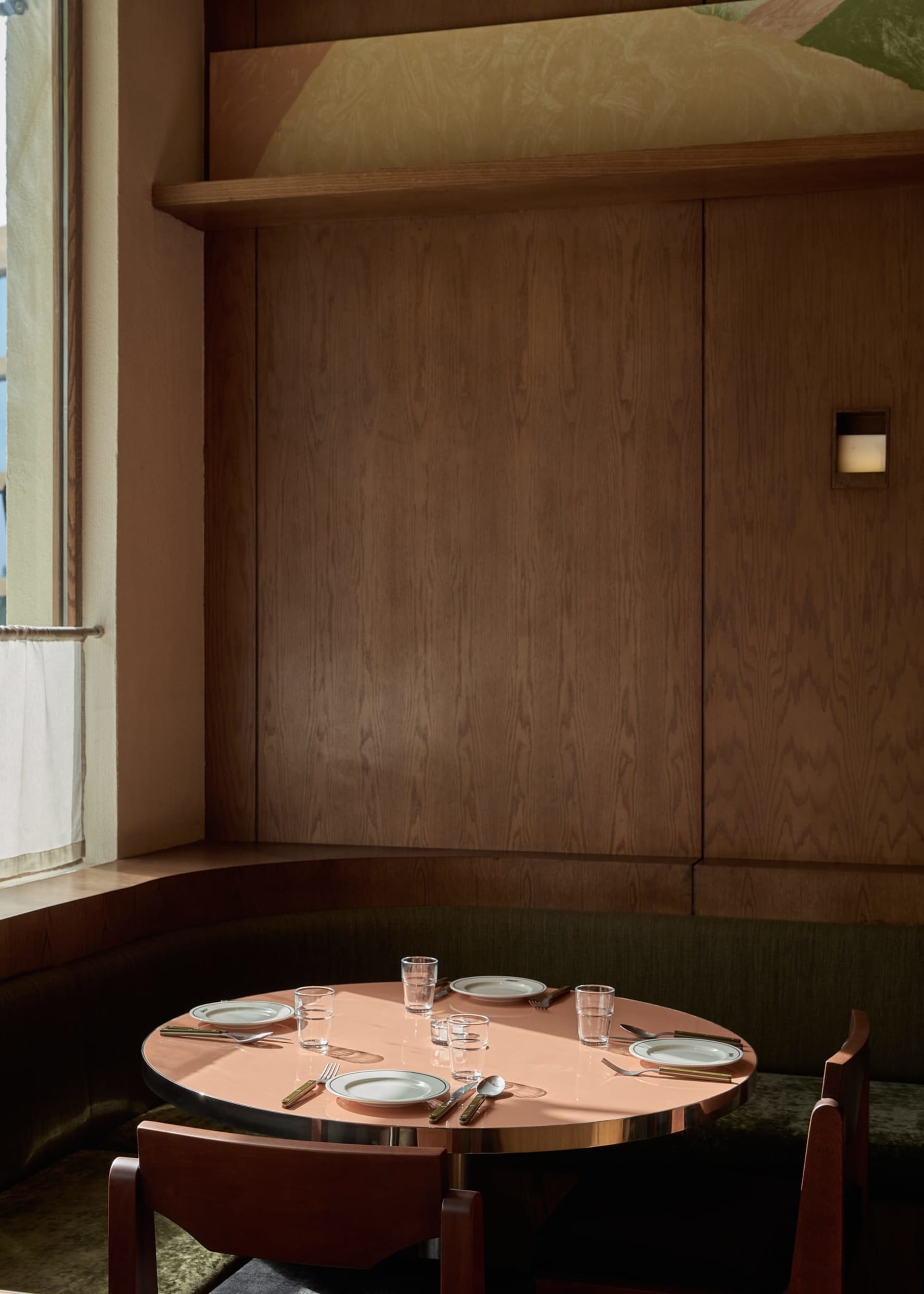 A dining room with a wooden table and chairs, set with plates, glasses, and cutlery, surrounded by a warm and inviting atmosphere with natural light from a window
