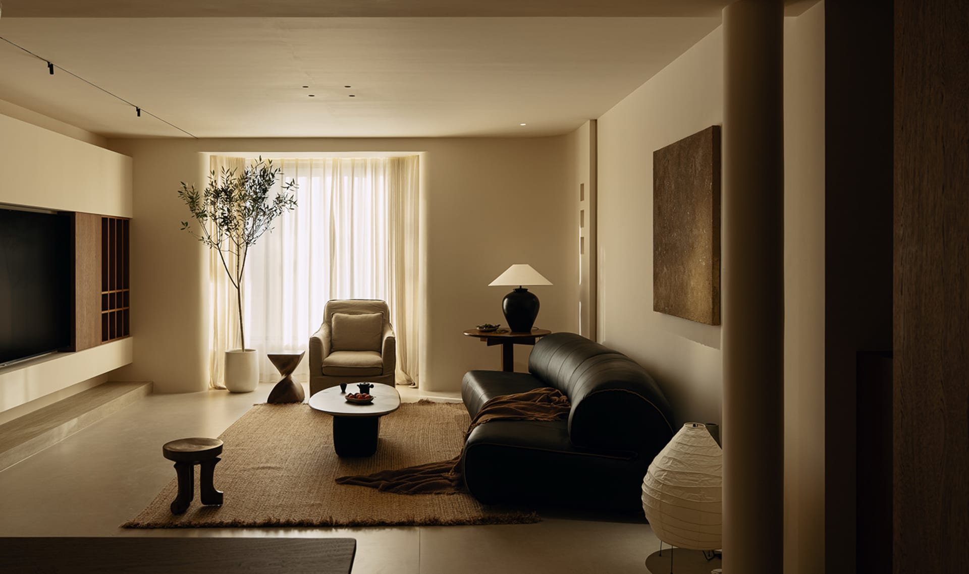 A well-lit living room with a black leather couch, chair, coffee table, and a potted plant, featuring a modern style with clean lines and minimalist design