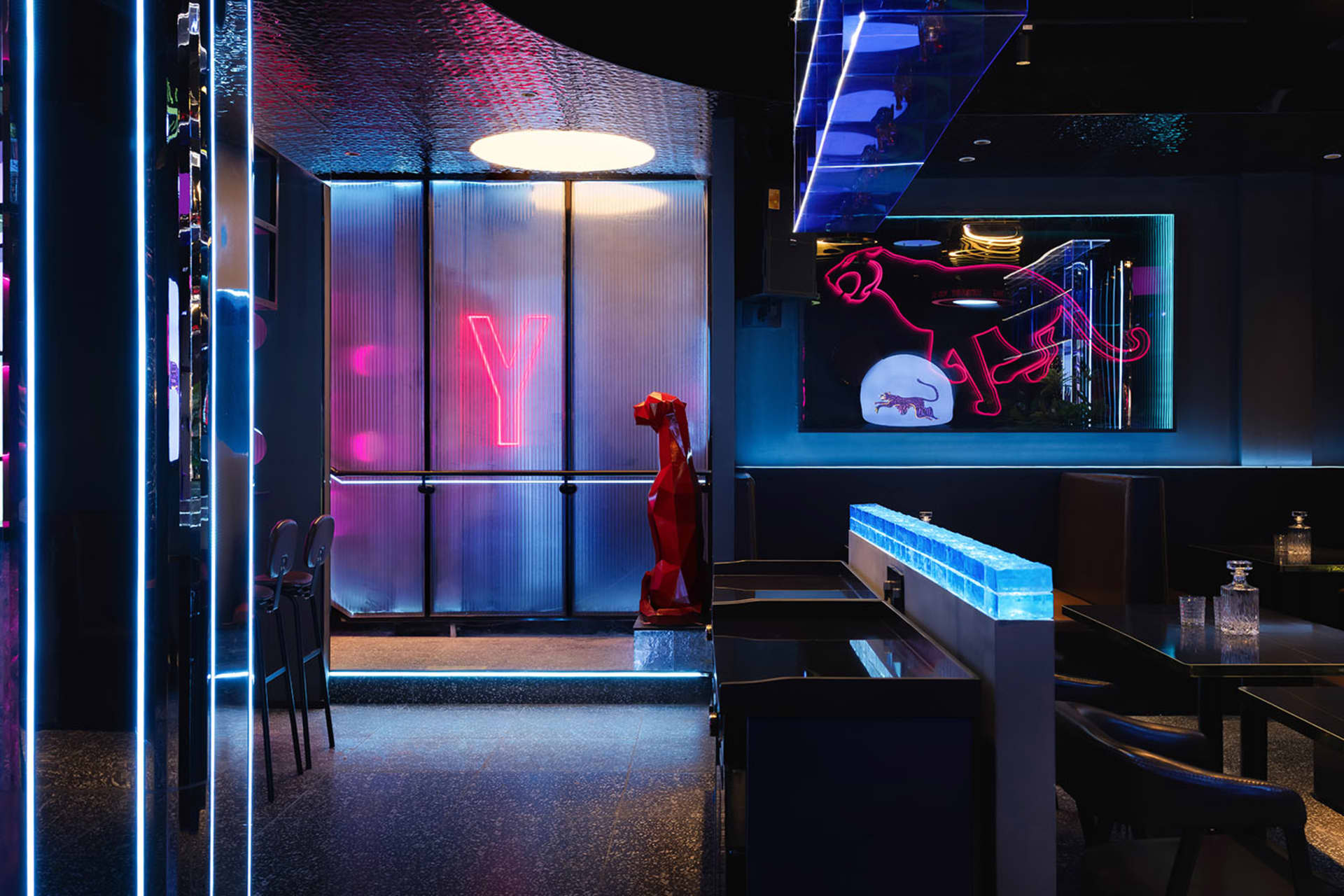 A modern restaurant with a blue and red color scheme, featuring a red robot statue and neon sign, comfortable seating, and dim lighting