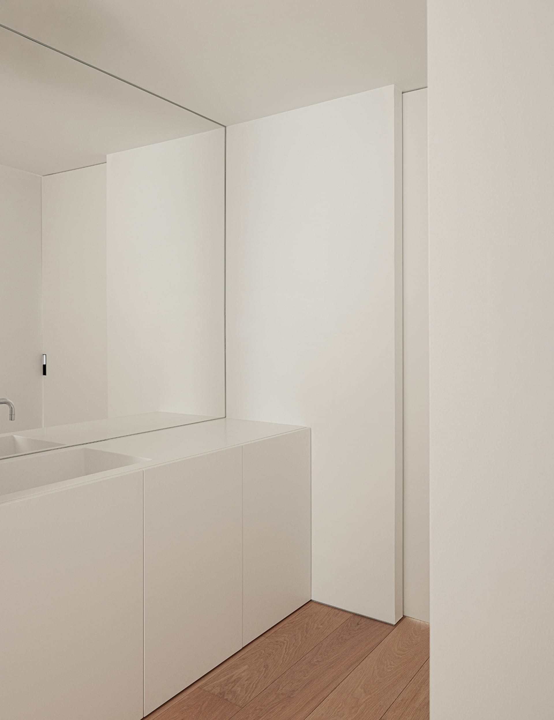 White bathroom with a sink under a mirror and a door in the background
