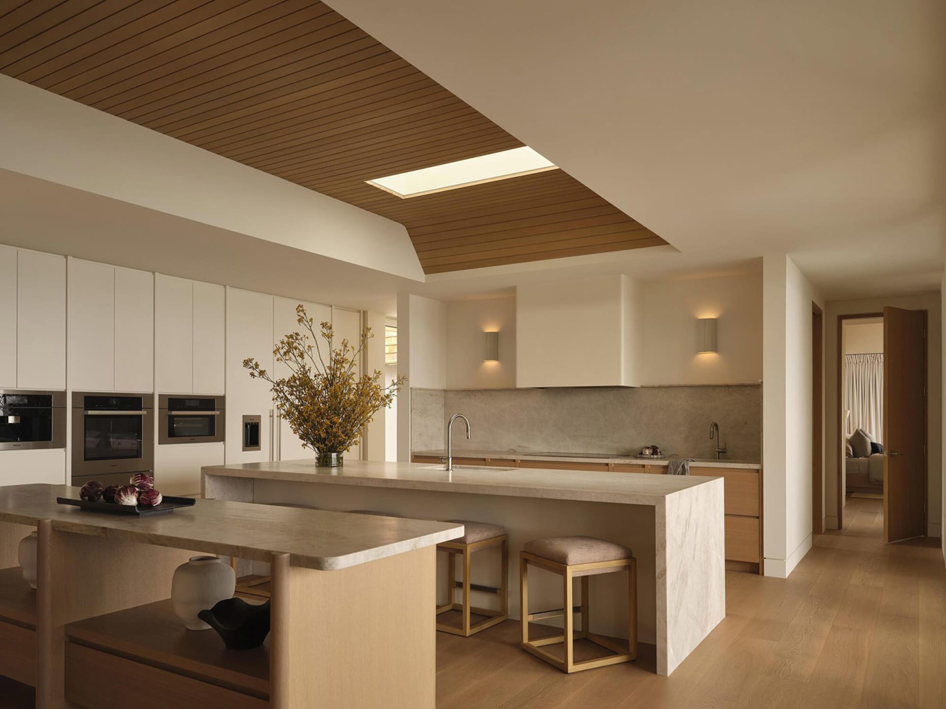A modern kitchen with a wooden floor and white cabinets, featuring a sink, refrigerator, and microwave, with dim lighting creating a cozy atmosphere
