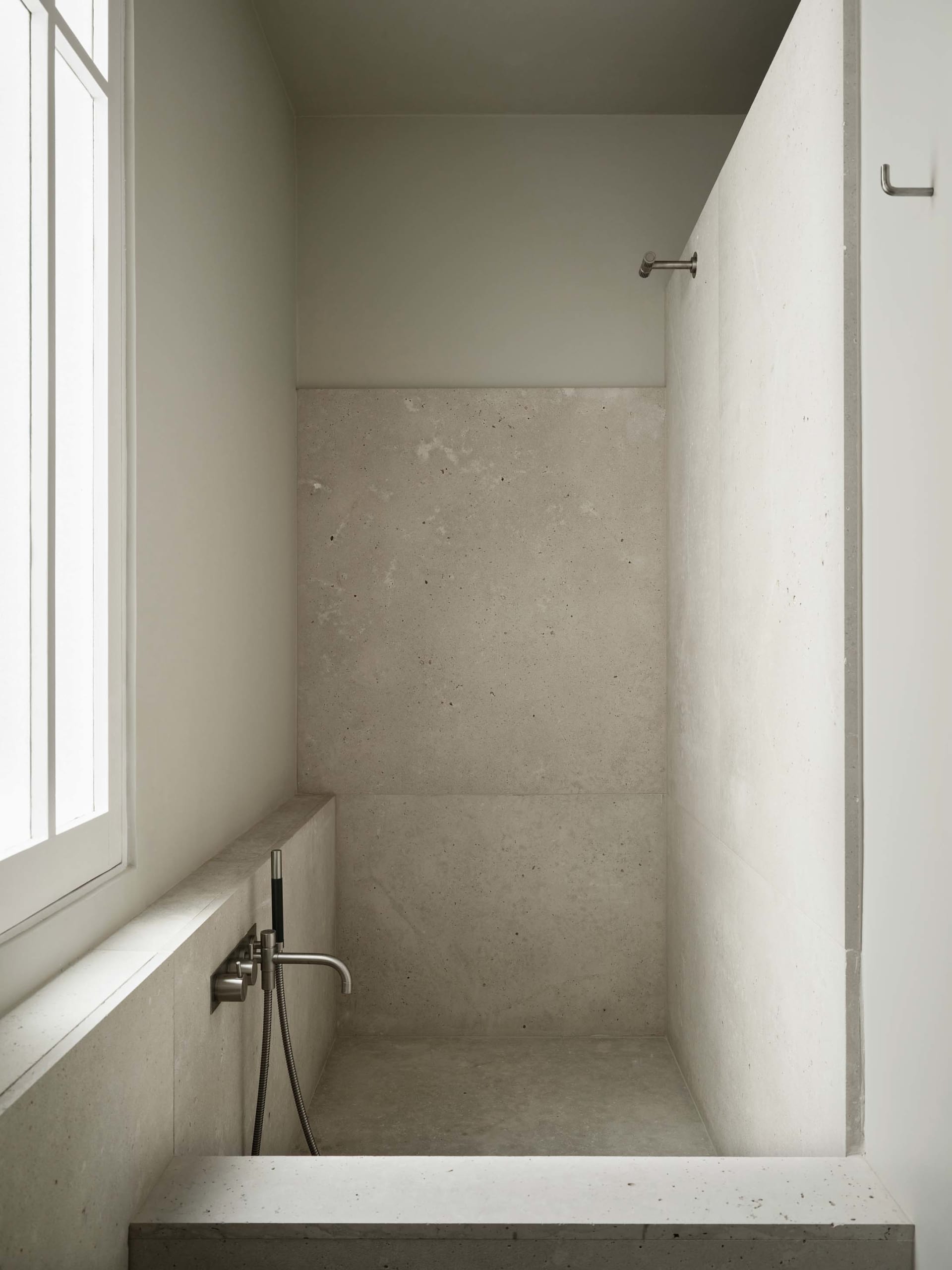 A clean bathroom with a white concrete shower stall and a window, well-maintained and minimalist