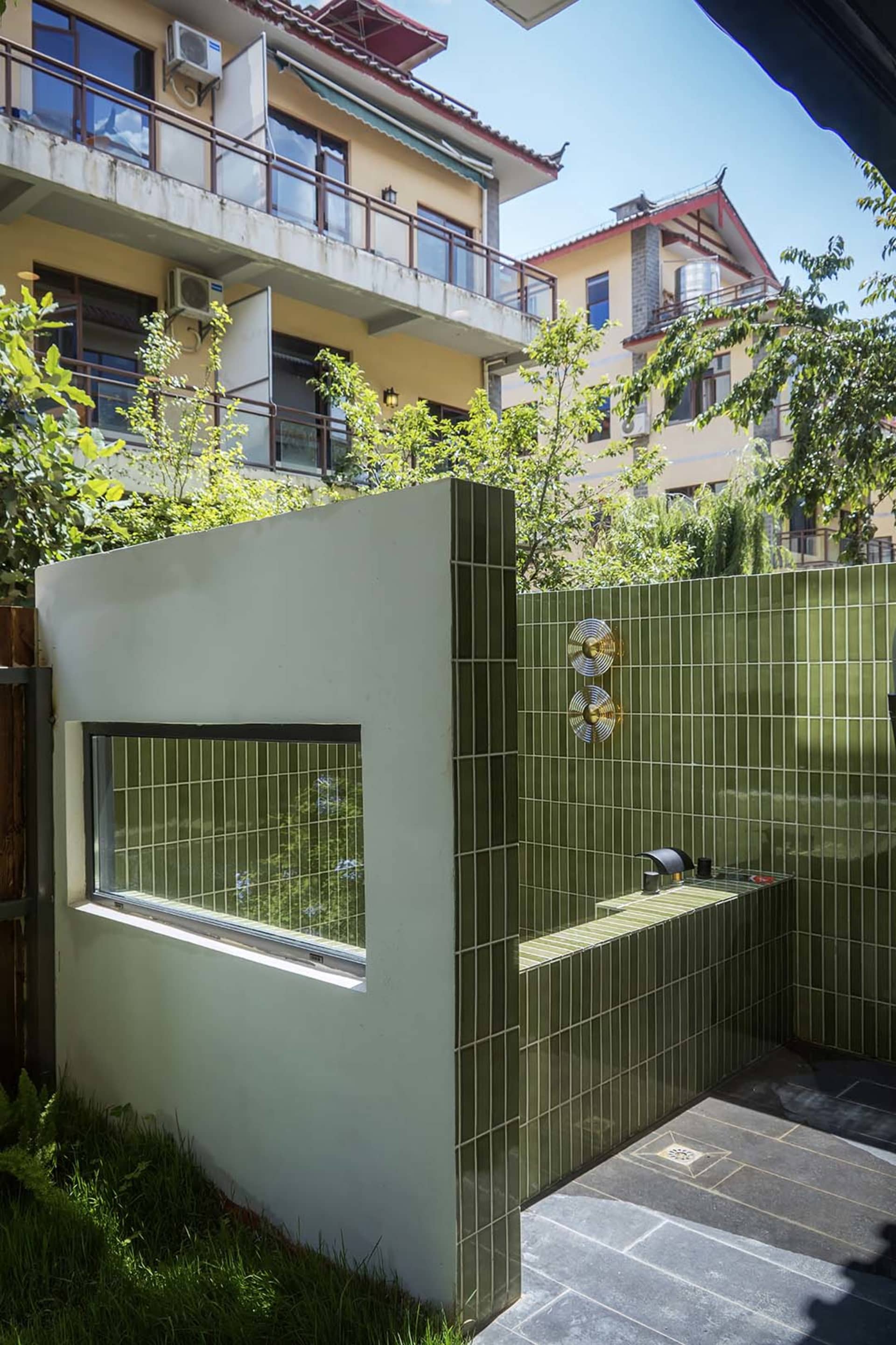 Bathroom with a green tile wall, a window, sink, and toilet, with natural light and modern style