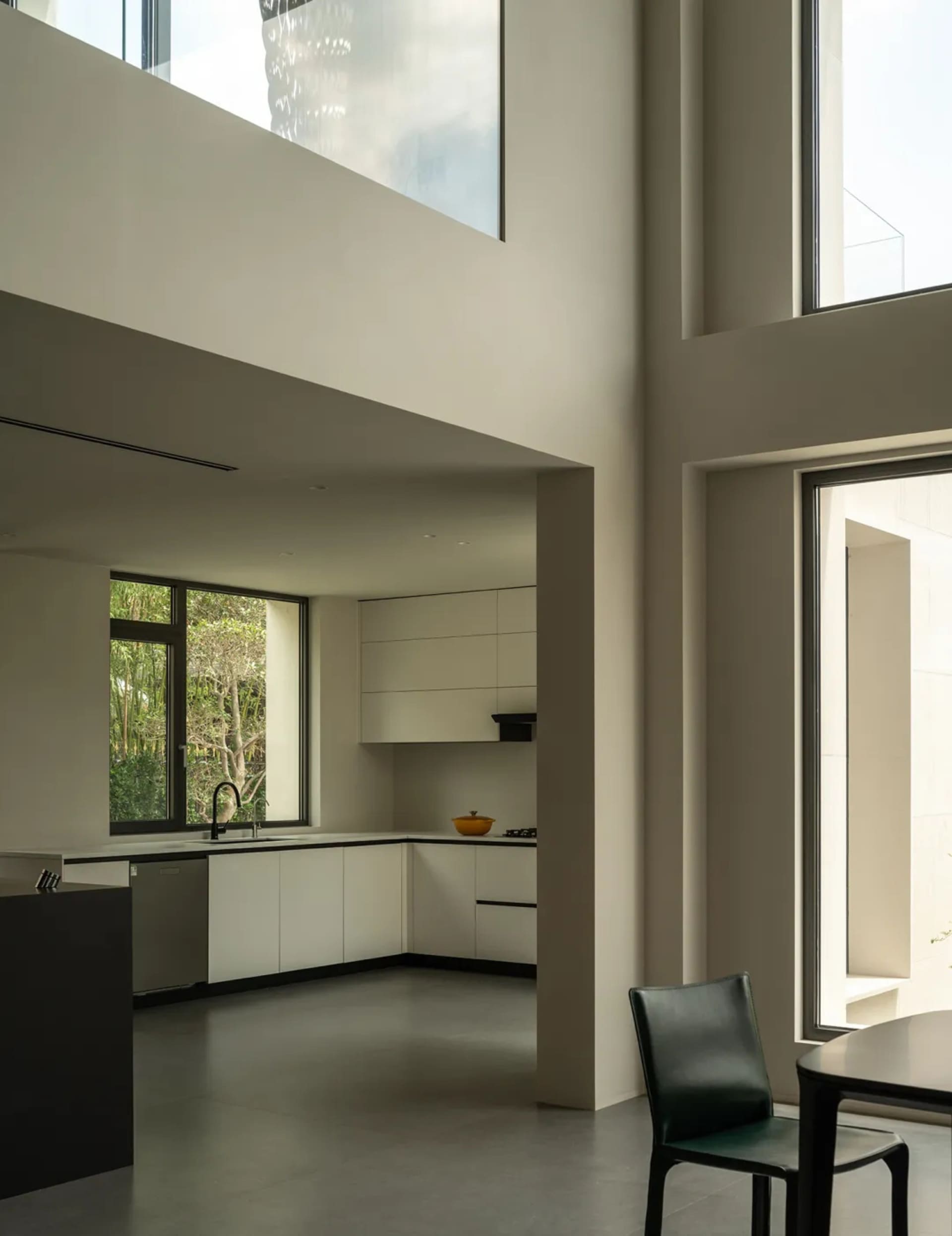 A modern kitchen and dining area with white walls, a dining table, chairs, a couch, and a chair, well-lit by natural light through windows