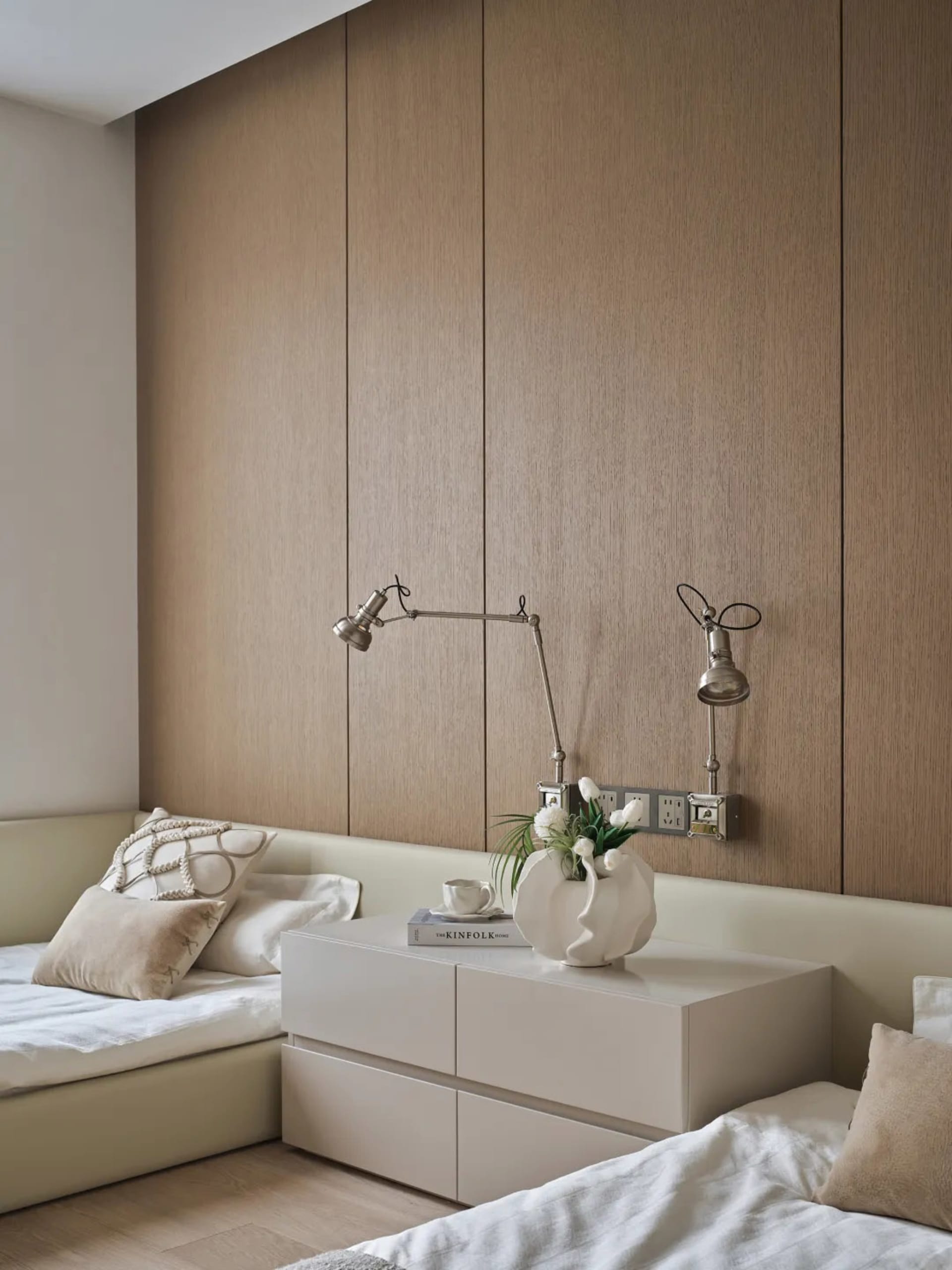 A well-lit bedroom with a bed, dresser, and lamp, featuring wood and white surfaces