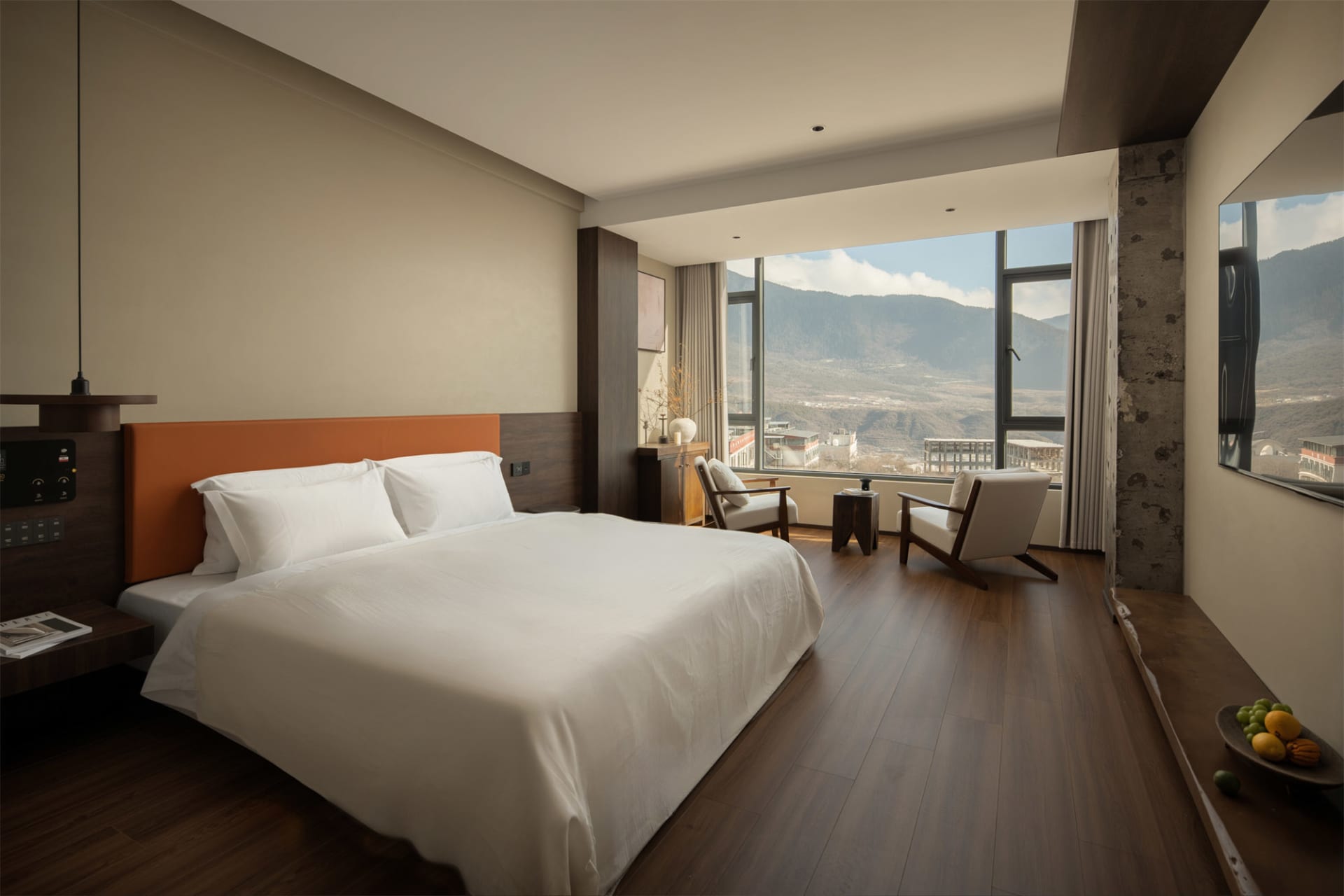 A well-lit bedroom with a wooden floor, a bed, a chair, and a table, near a window