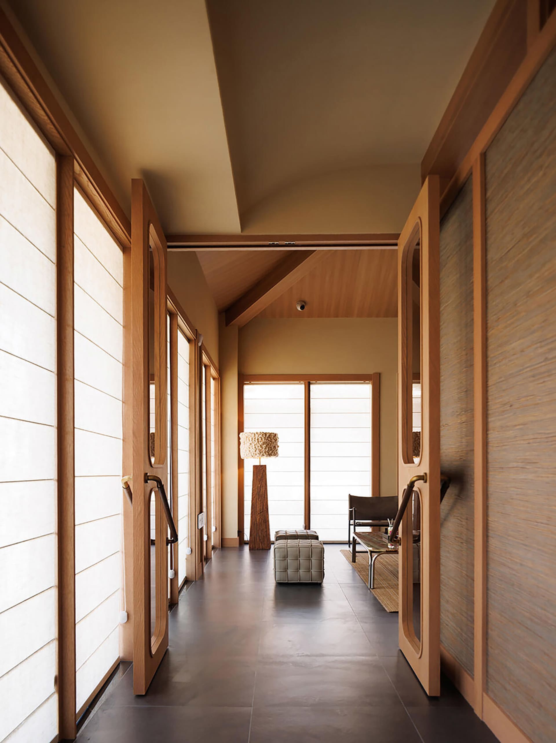 A living room with a wooden floor, a couch, a chair, and a lamp, lit by natural sunlight through the windows