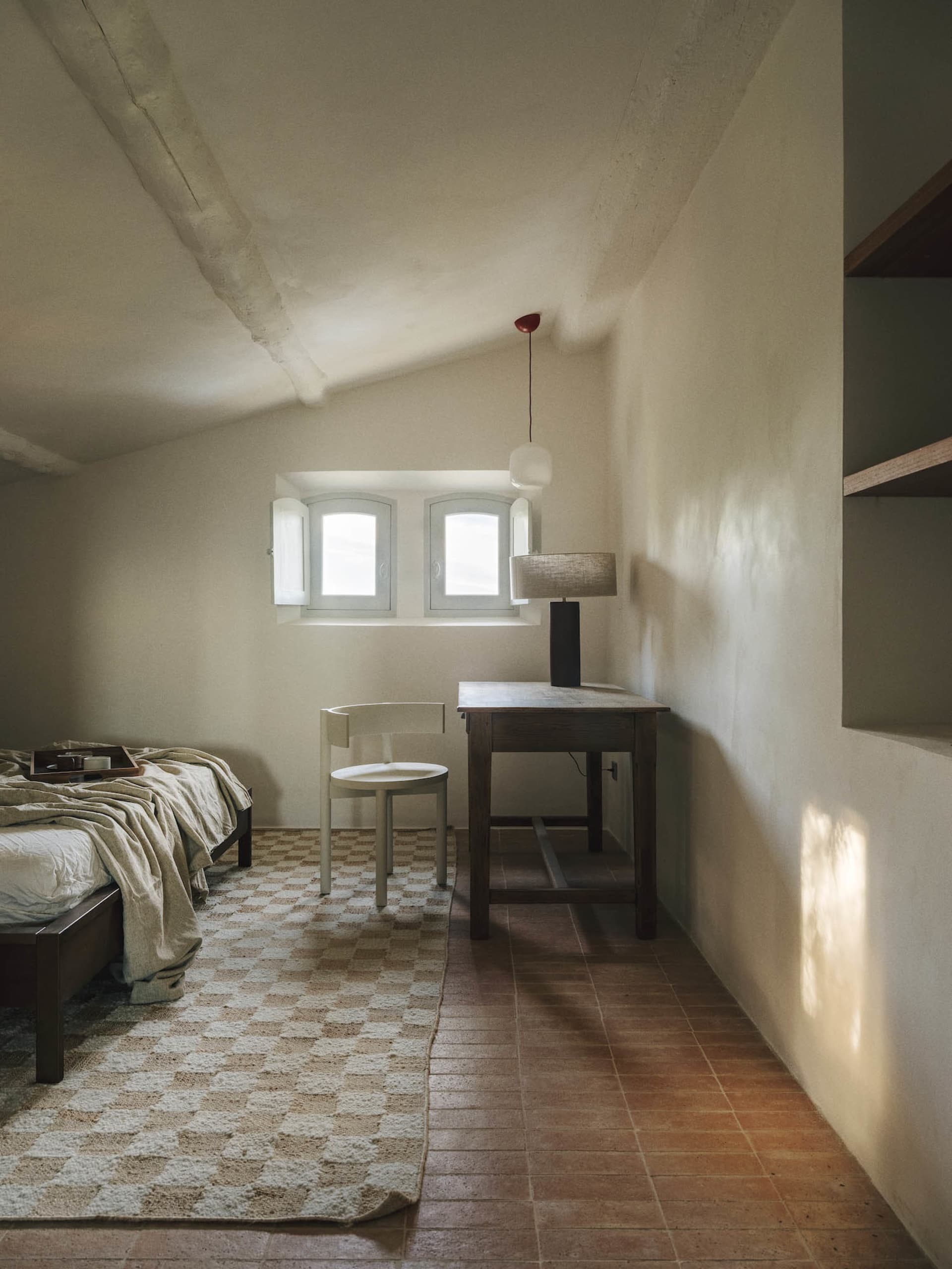 A well-lit bedroom with a bed, chair, and desk, featuring a white color scheme and wooden furniture