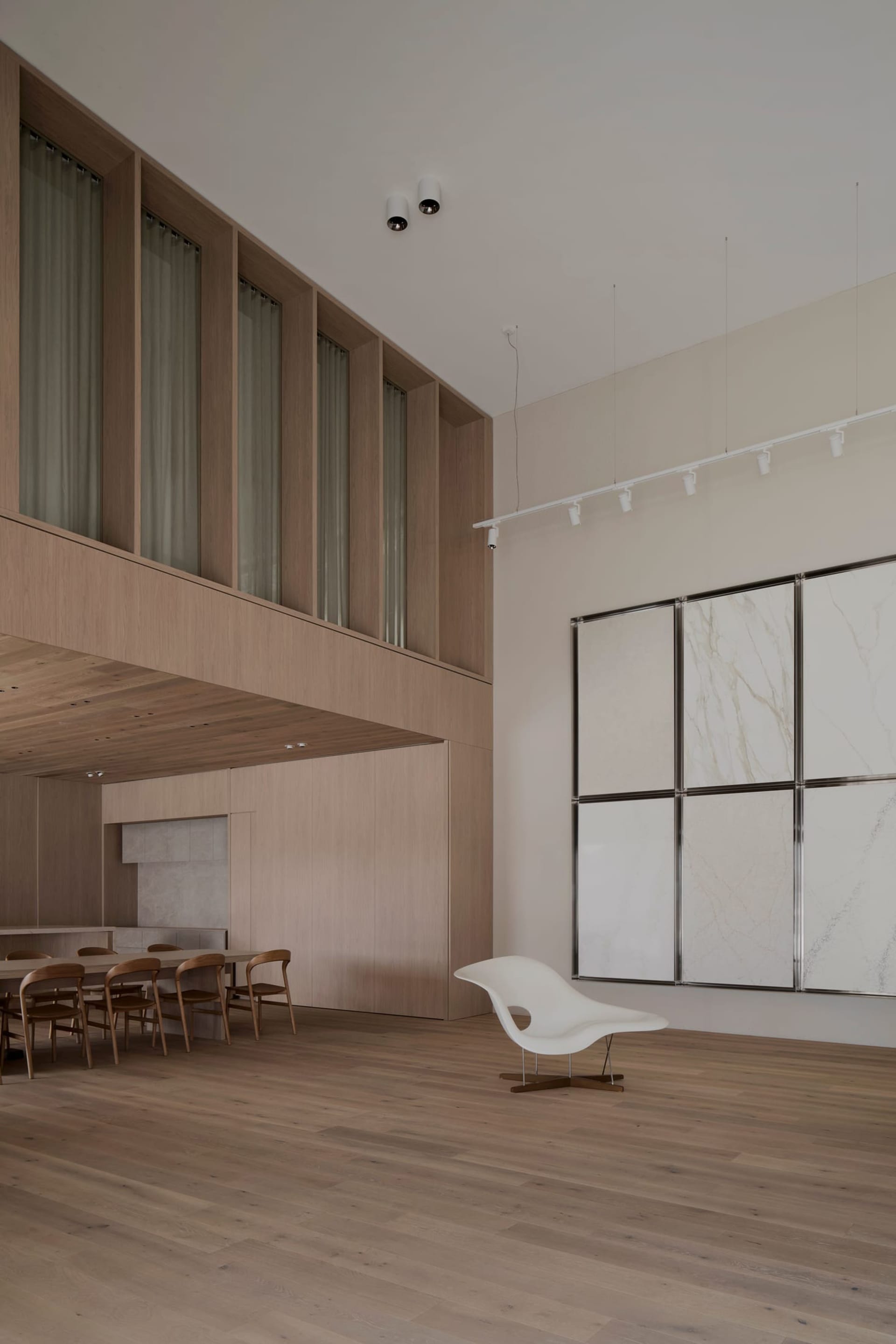 Modern living room with wooden floors, a white wall with a painting, a dining table, a couch, and natural light from windows