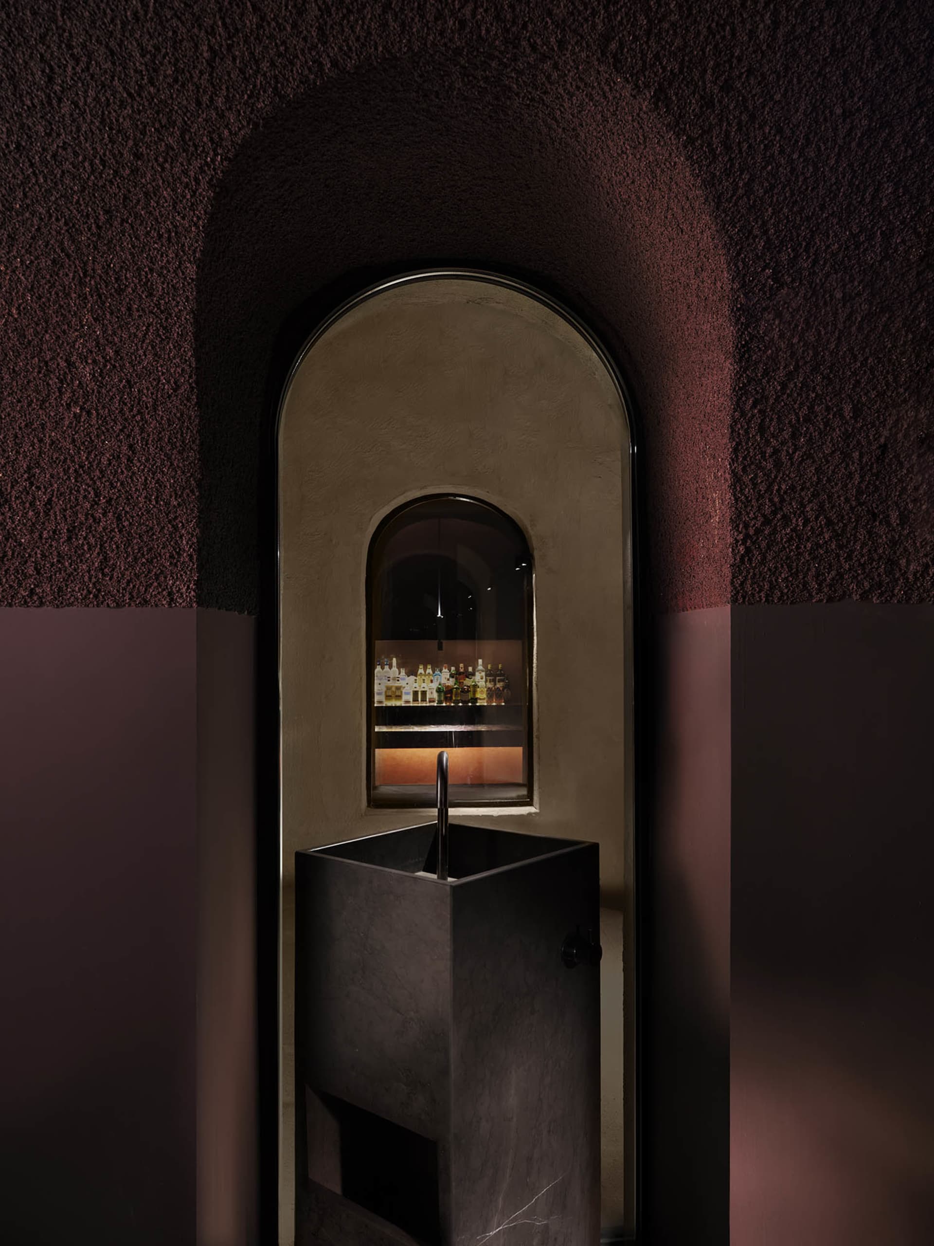 Bathroom with a metal sink and mirror in a dimly lit room with a red wall and brown floor