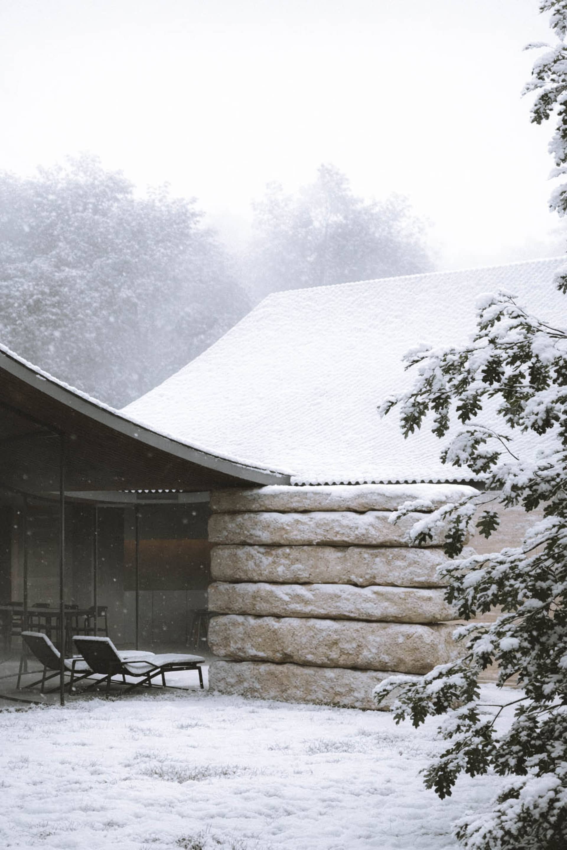 一座雪覆蓋的房子，曲線屋頂和石牆，融合現代和傳統建築風格