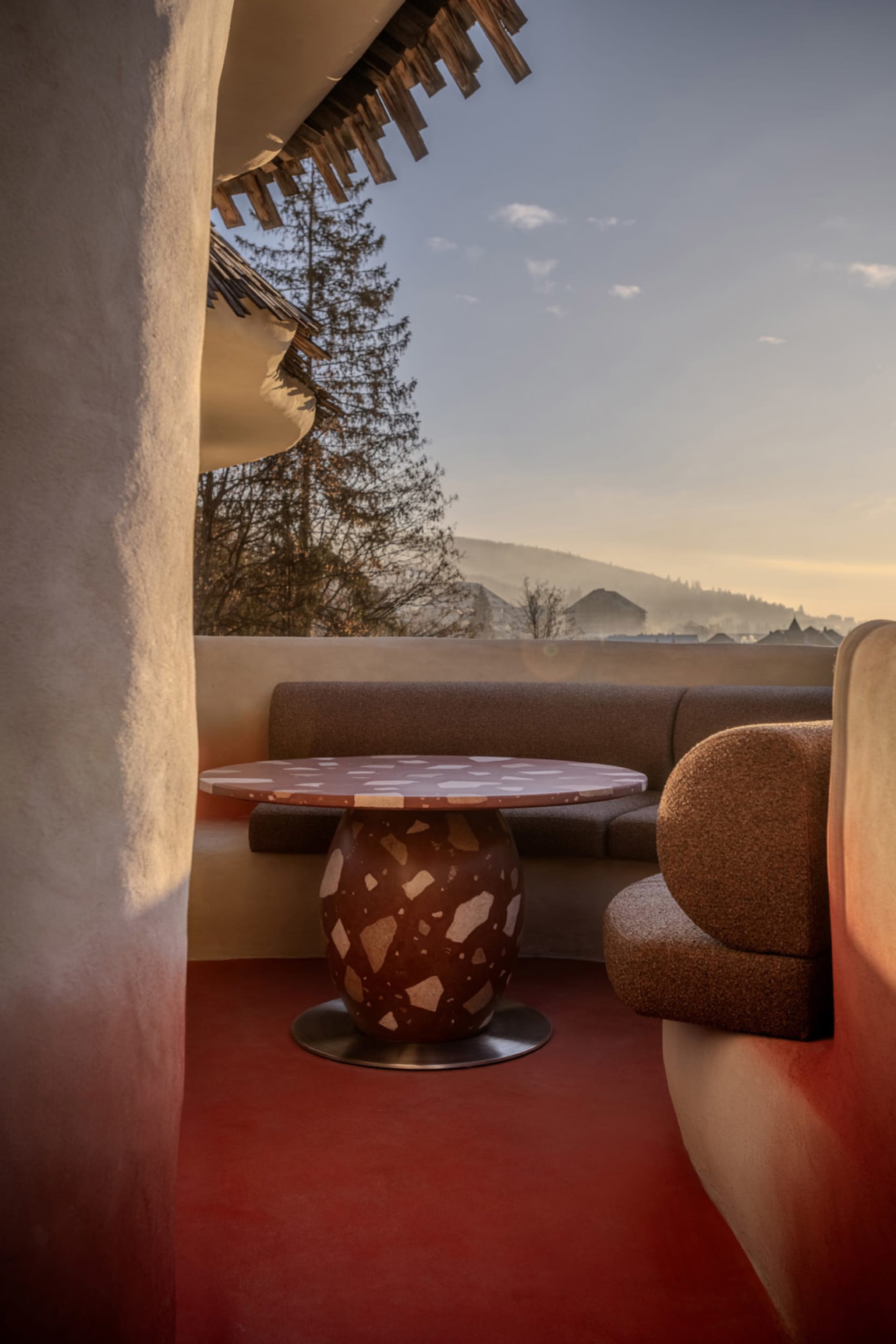 A well-lit living room with a red floor, a couch, a chair, and a dining table, creating a warm and inviting atmosphere