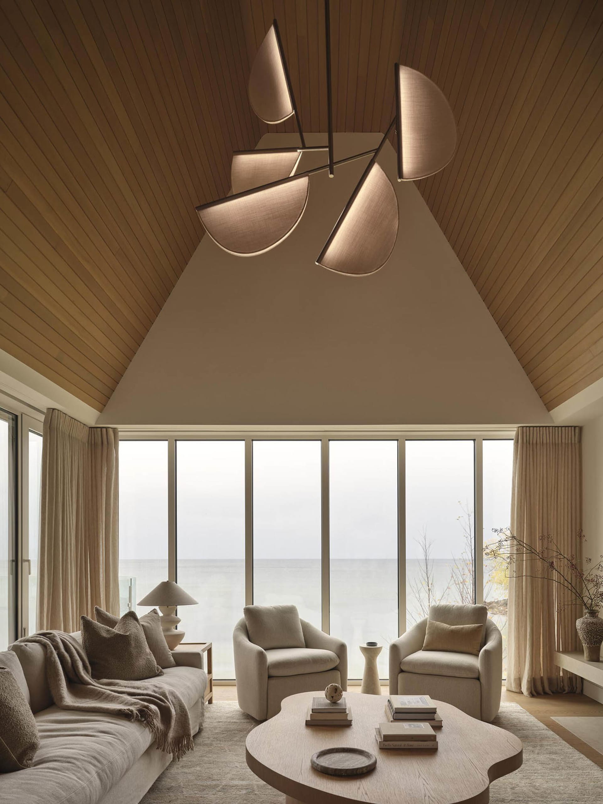 Bright and welcoming living room with a large window, a couch, a chair, and a dining table, surrounded by modern furniture and natural light