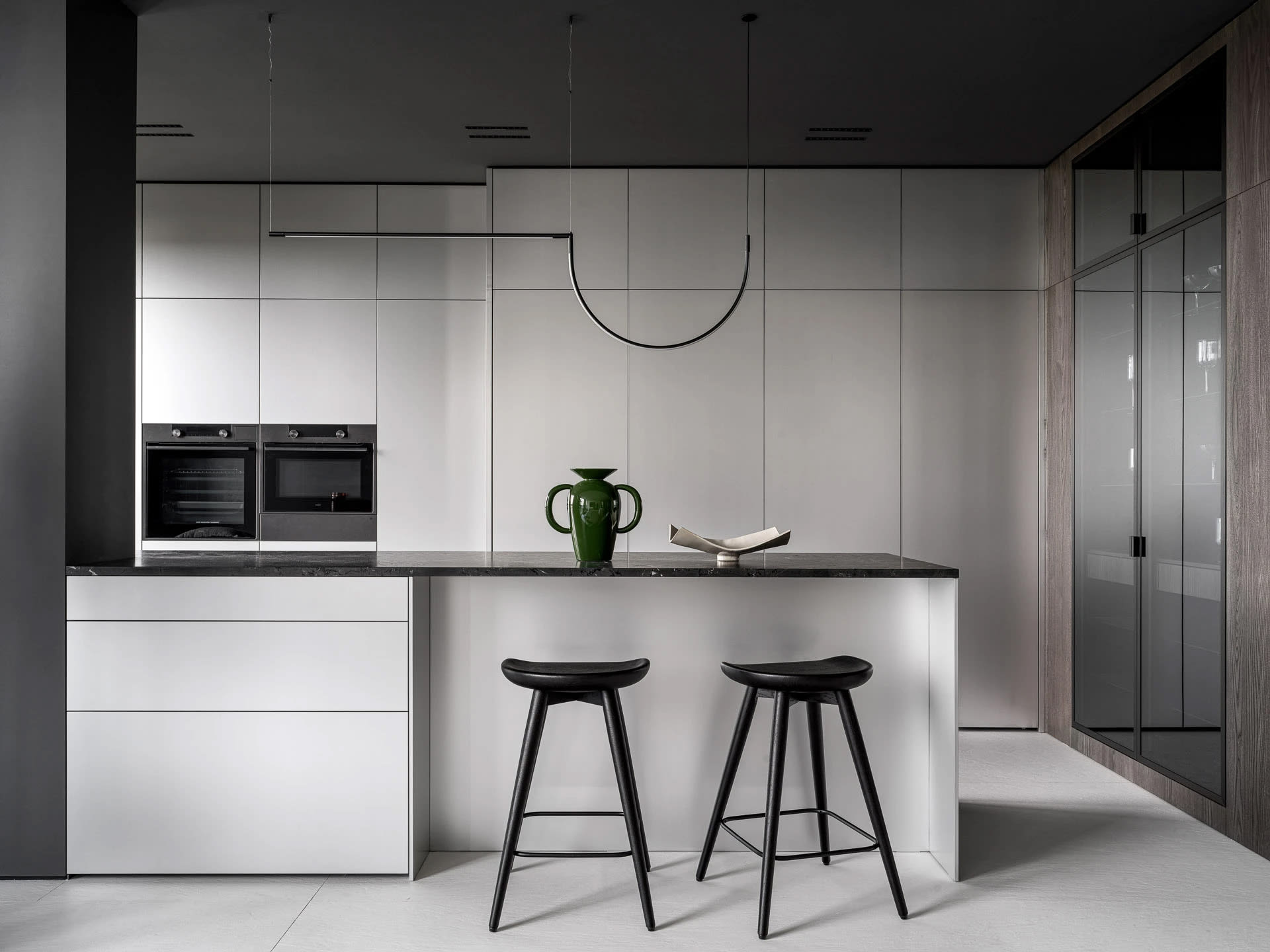 Modern kitchen with a black and white color scheme, featuring white cabinets, black countertops, and a green vase and book on the countertop