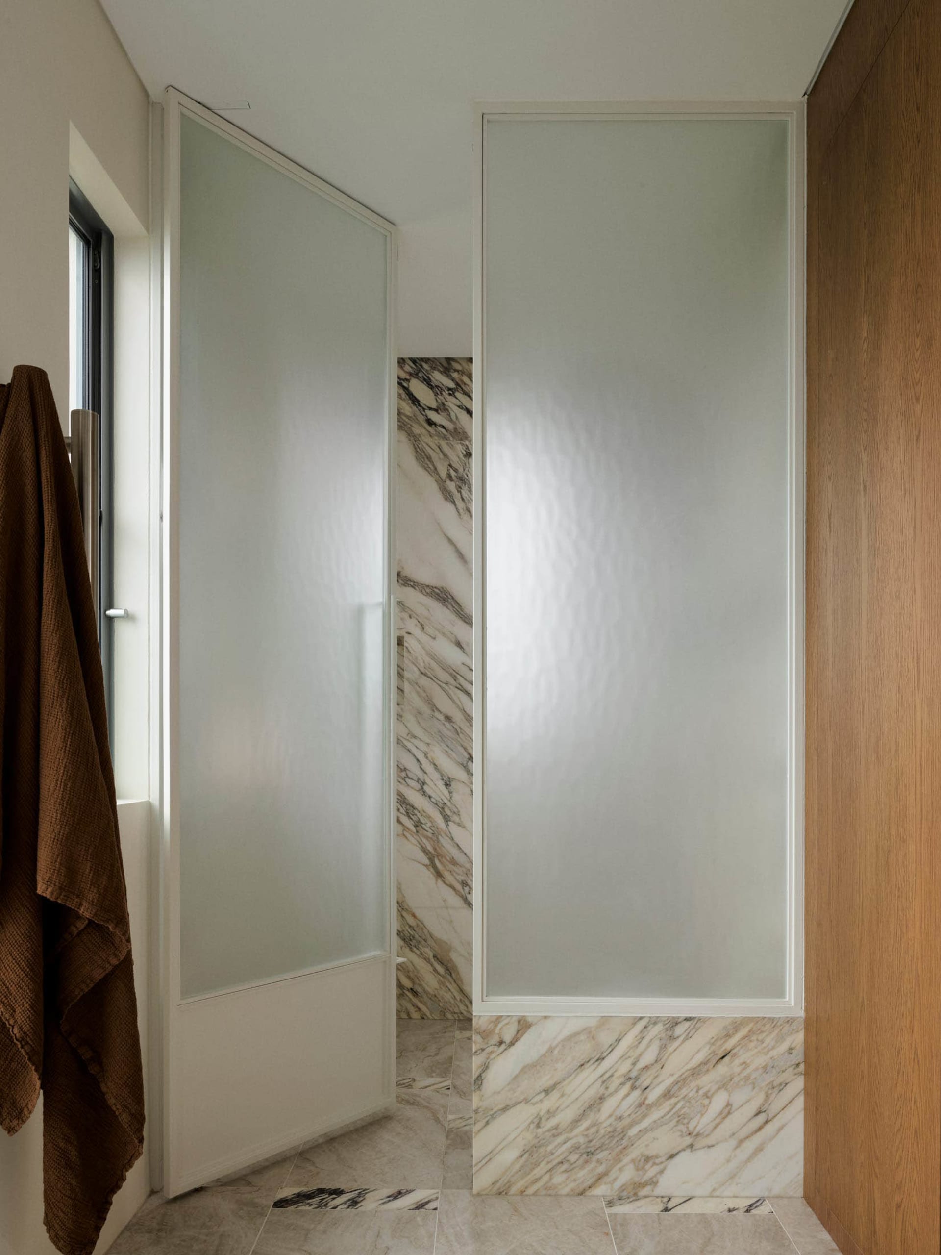 Bathroom with a marble-like shower stall, glass enclosure, and natural light from a window