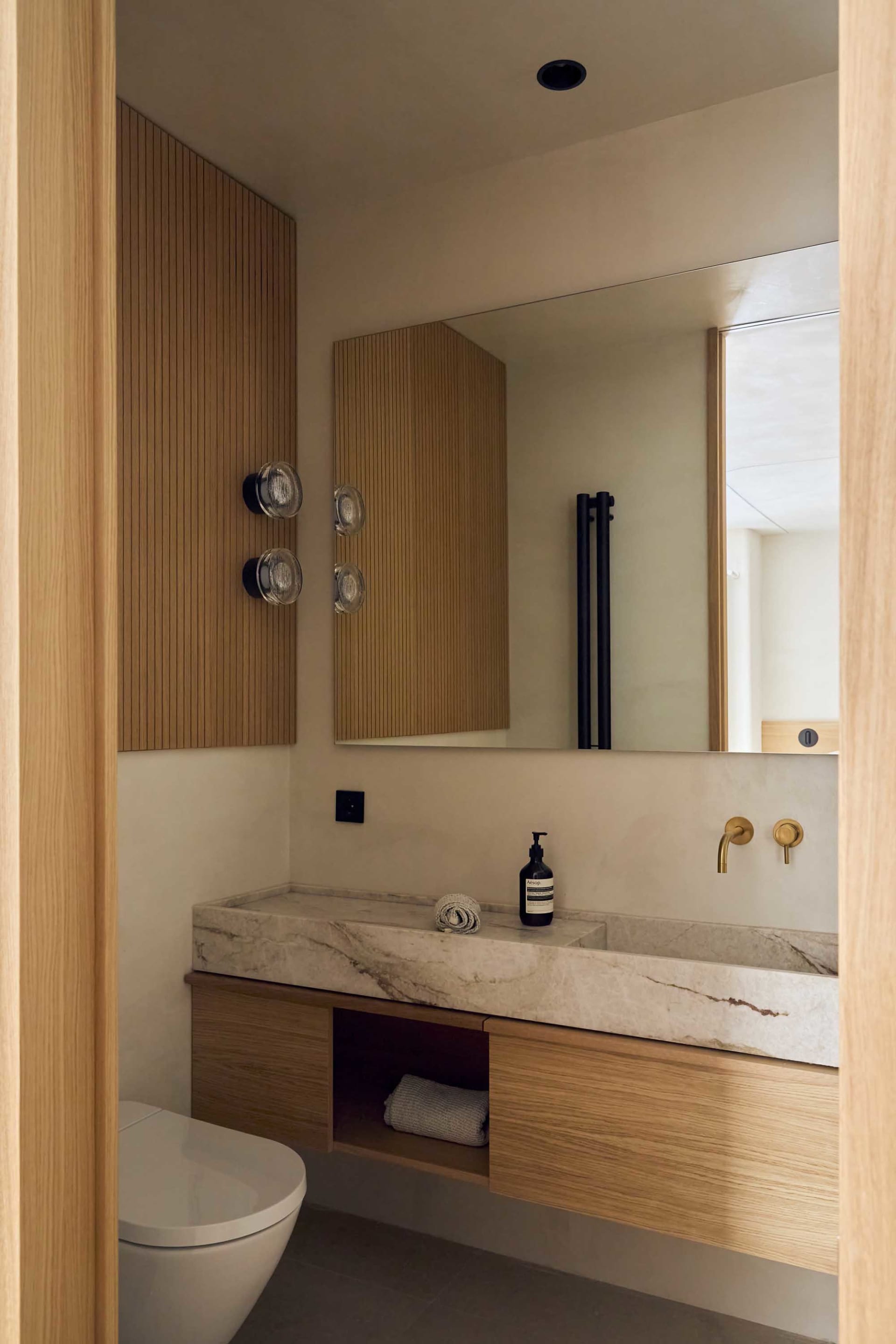 Bathroom with a marble sink, wooden cabinet, and large mirror, featuring modern and clean design with natural light and warm tones