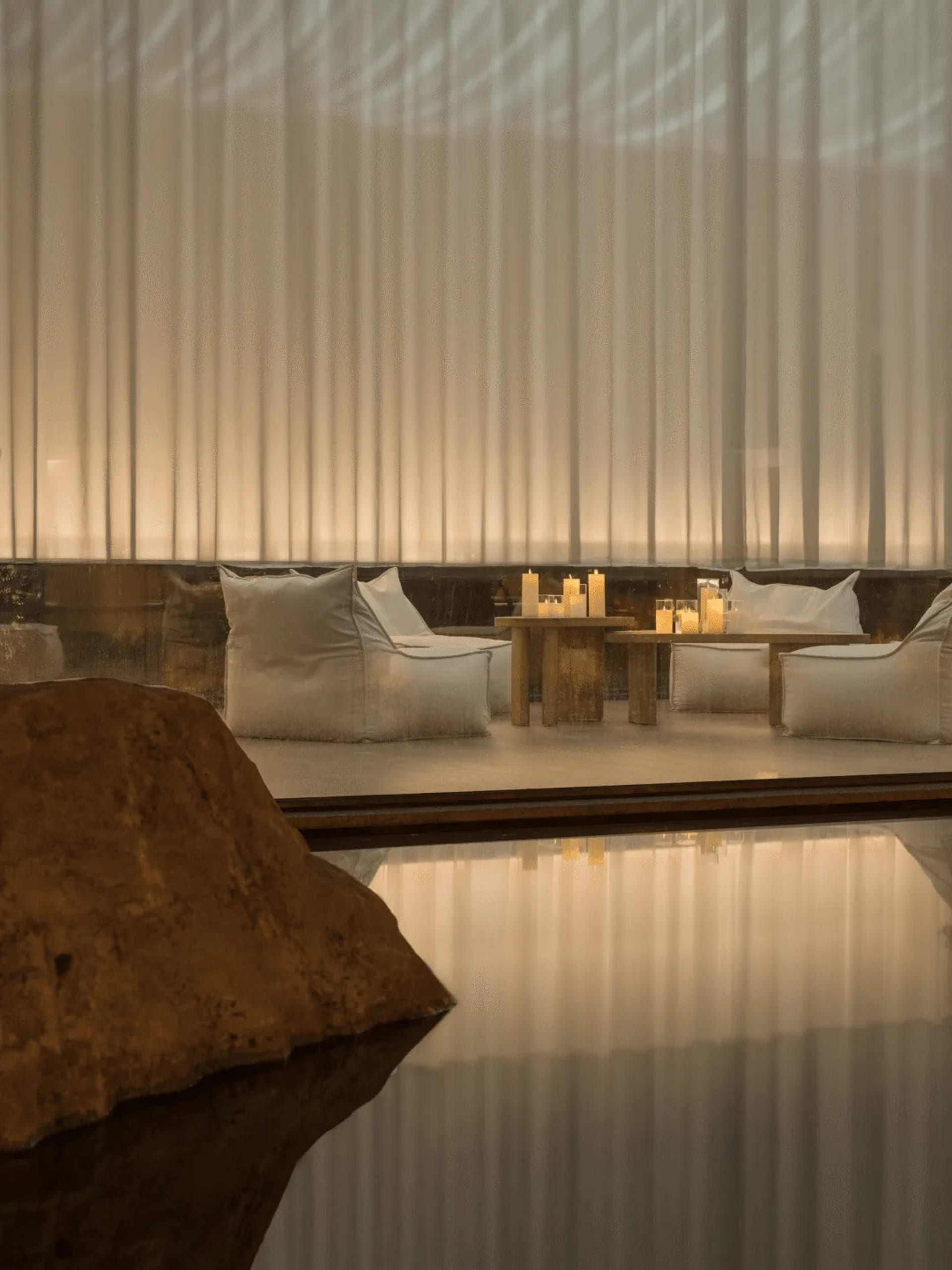 A modern dining space with a wooden table and chairs, surrounded by candles and natural light from a nearby window