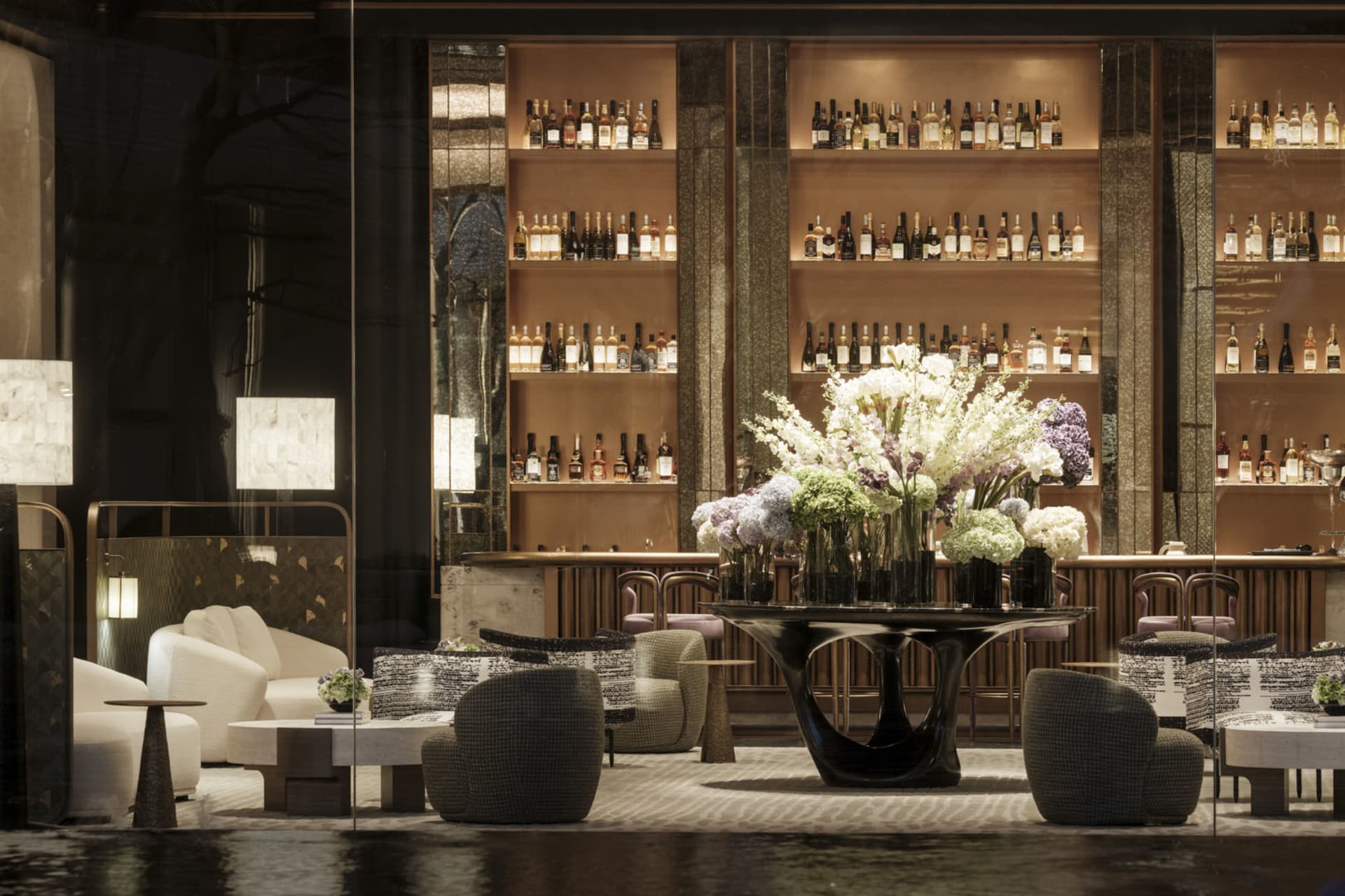A modern bar area with a large vase of flowers, comfortable seating, and a sophisticated atmosphere, decorated with bottles and a potted plant