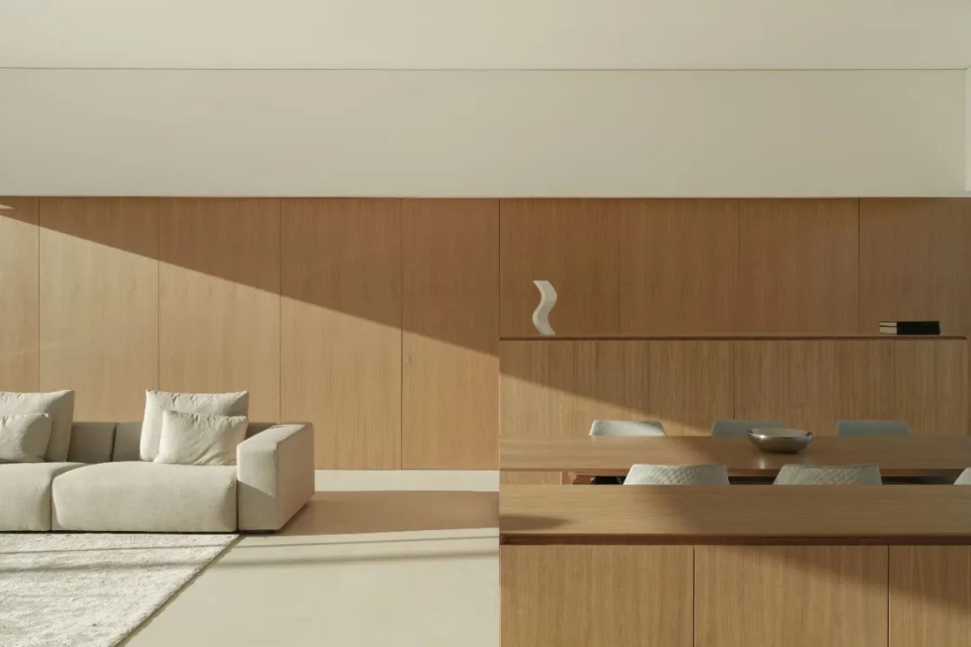 A modern living and dining area with a wooden floor, white walls, and natural light, featuring a couch, chair, dining table, and chairs with a bowl on the table