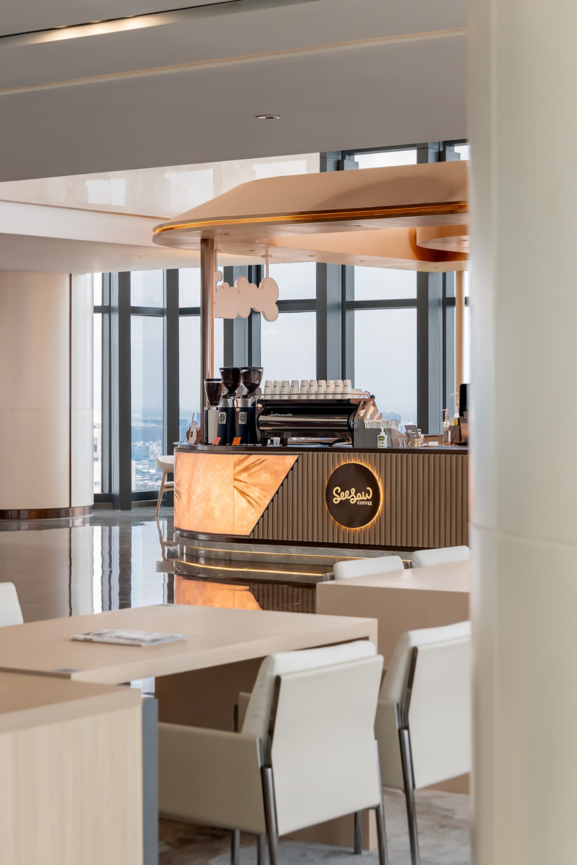 A modern coffee shop with a wooden counter and marble top, featuring a prominent coffee machine in a well-lit and inviting atmosphere