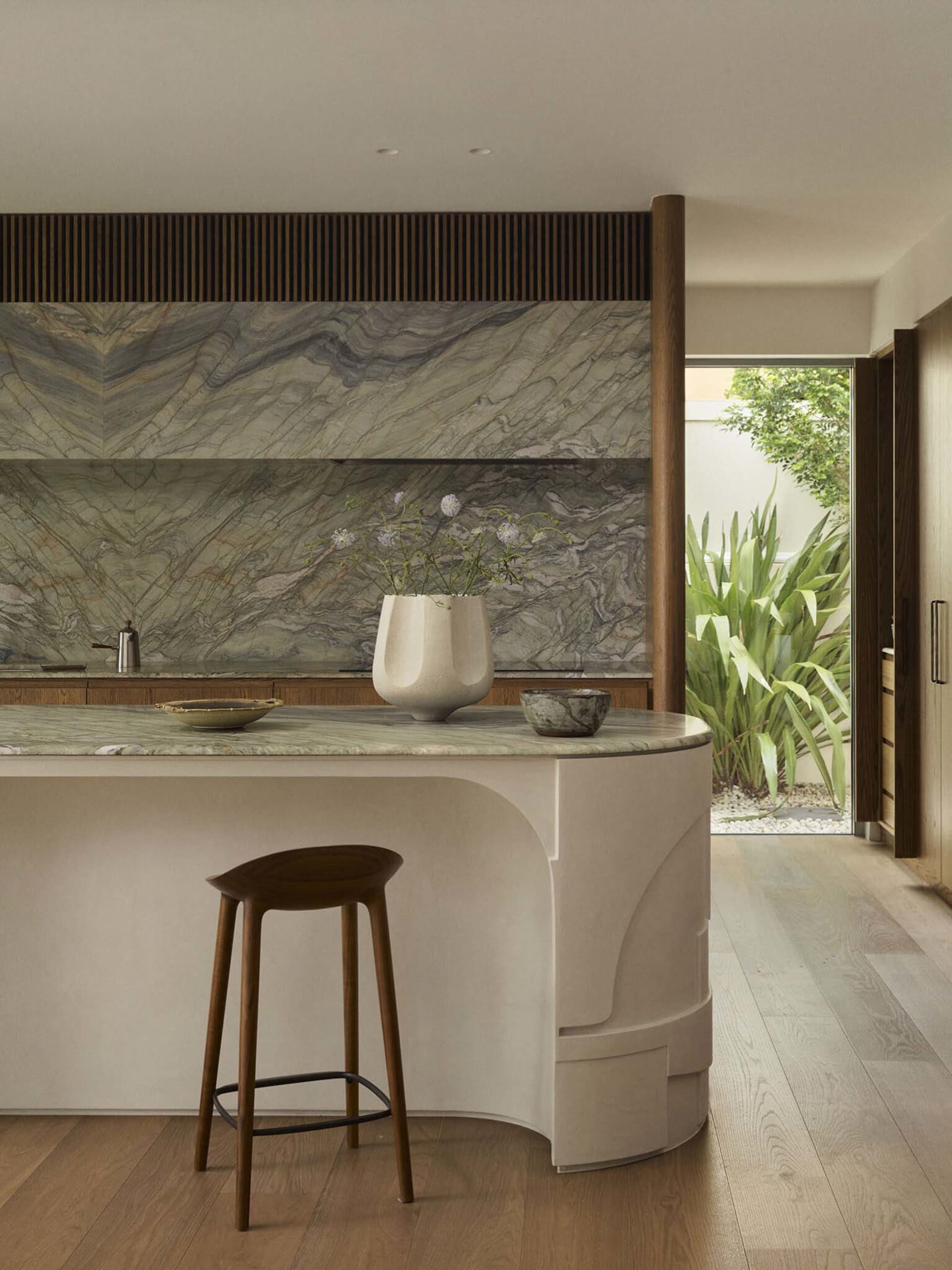 Modern kitchen with a white marble countertop, brown stools, and natural light from the windows