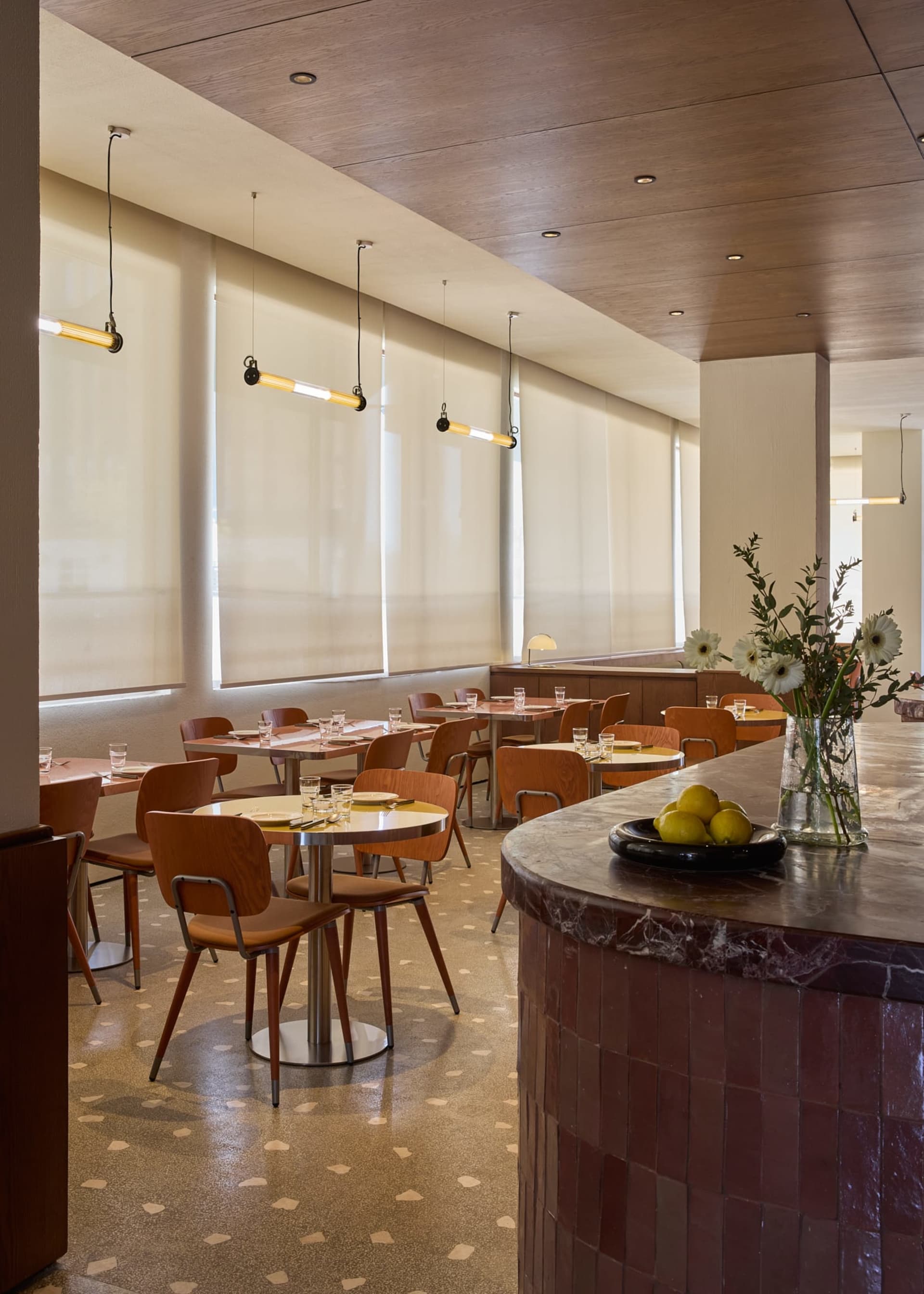 A modern restaurant interior with a dining area and bar featuring wood and marble materials, natural lighting, and a warm atmosphere