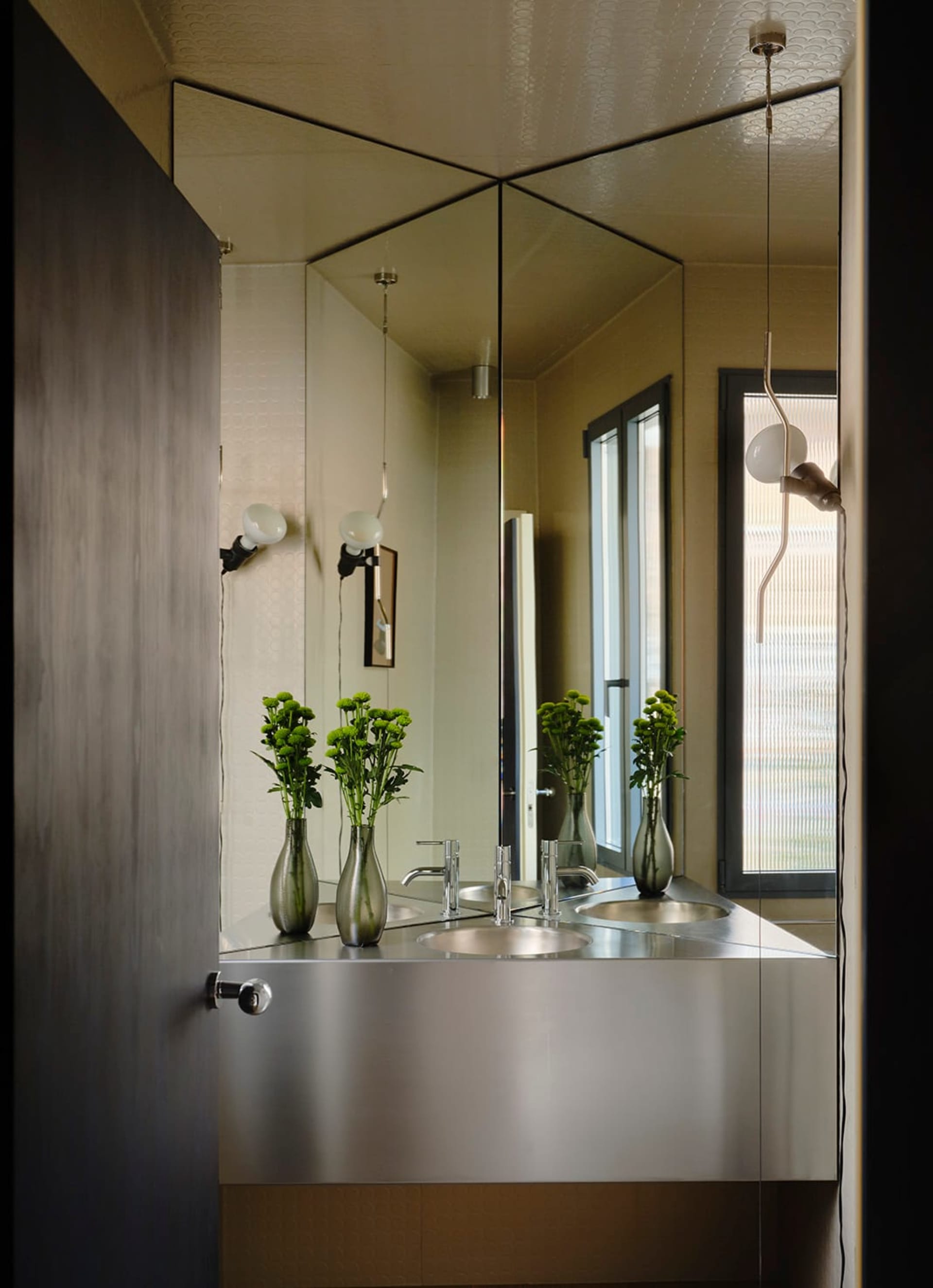 Modern bathroom with a metal sink and large mirror, natural light from a window, and dim lighting creating a cozy atmosphere