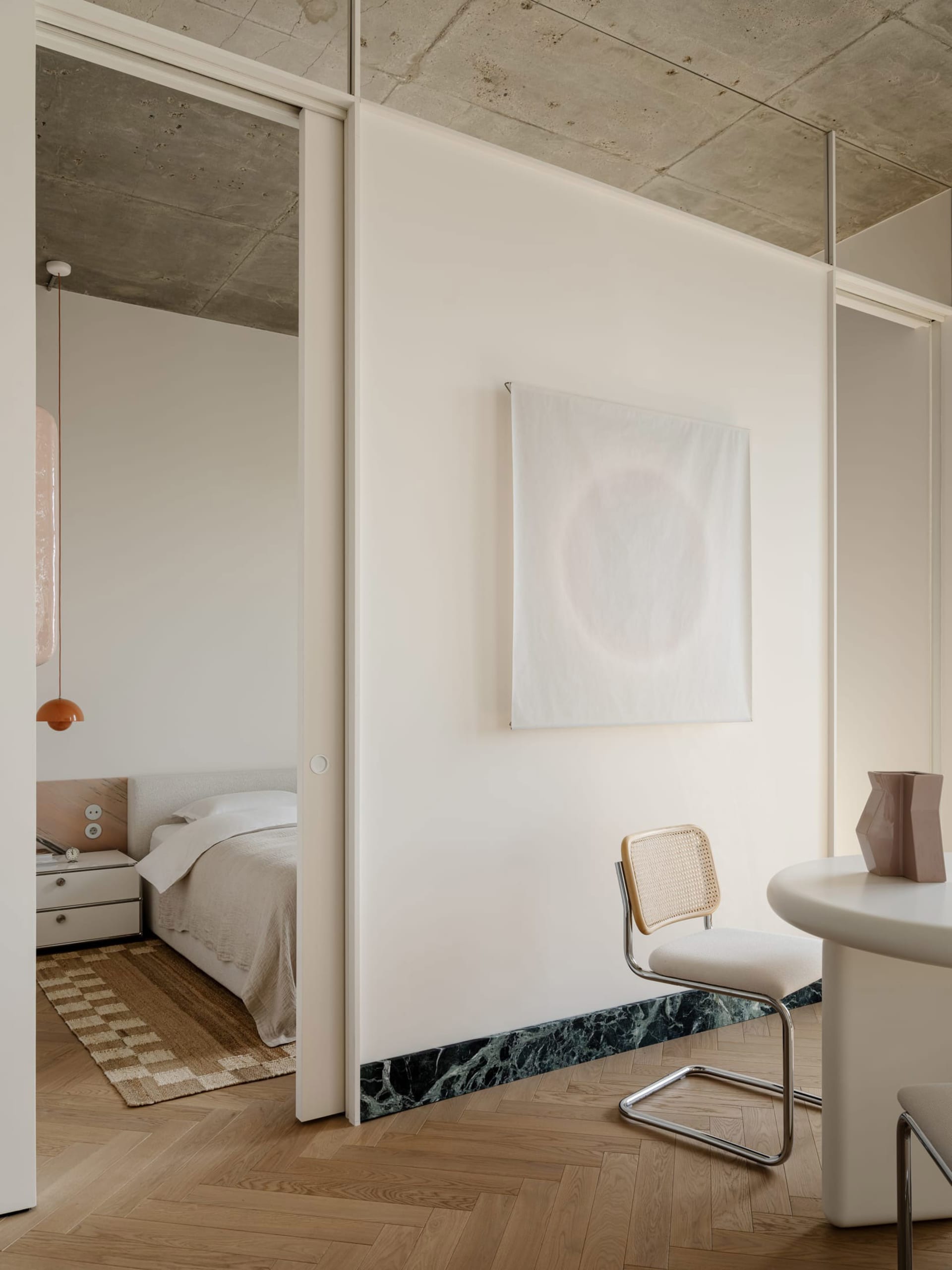 A modern bedroom with a white color scheme, a marble countertop, and a bed positioned against the wall, accompanied by a chair and a table in a functional arrangement