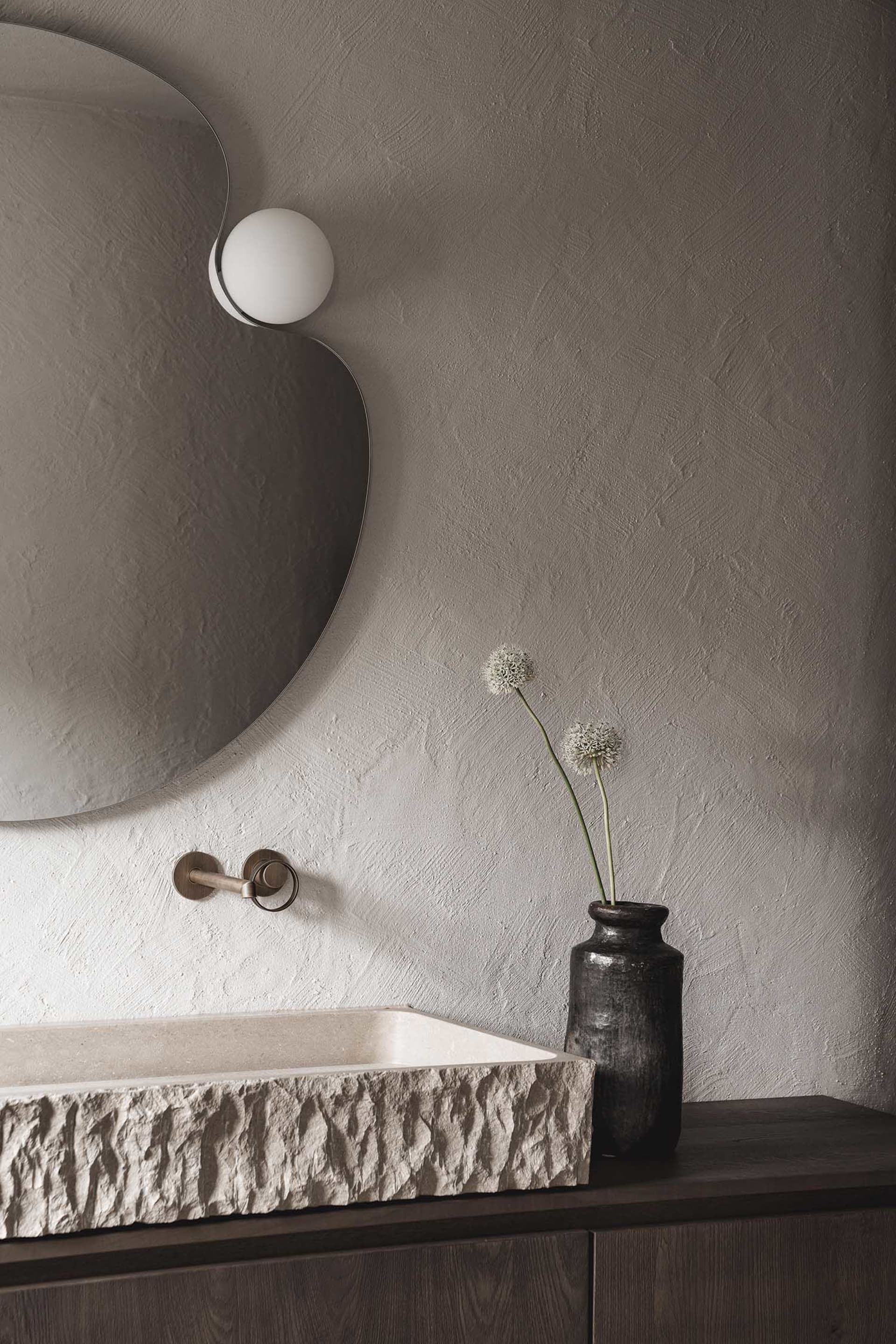 A modern bathroom with a sink, mirror, and vase with a flower, set against a bright and inviting background