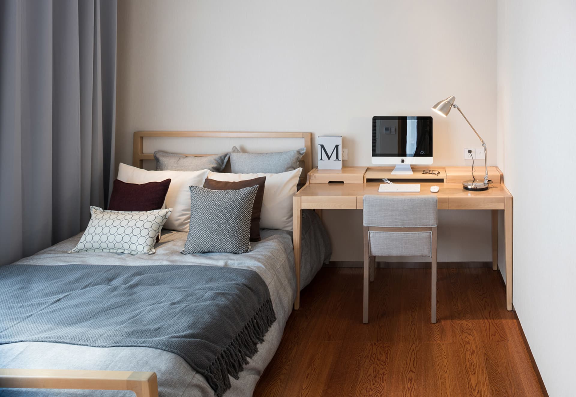 Cozy bedroom with a bed, desk, and chair, featuring a wooden floor and dim lighting