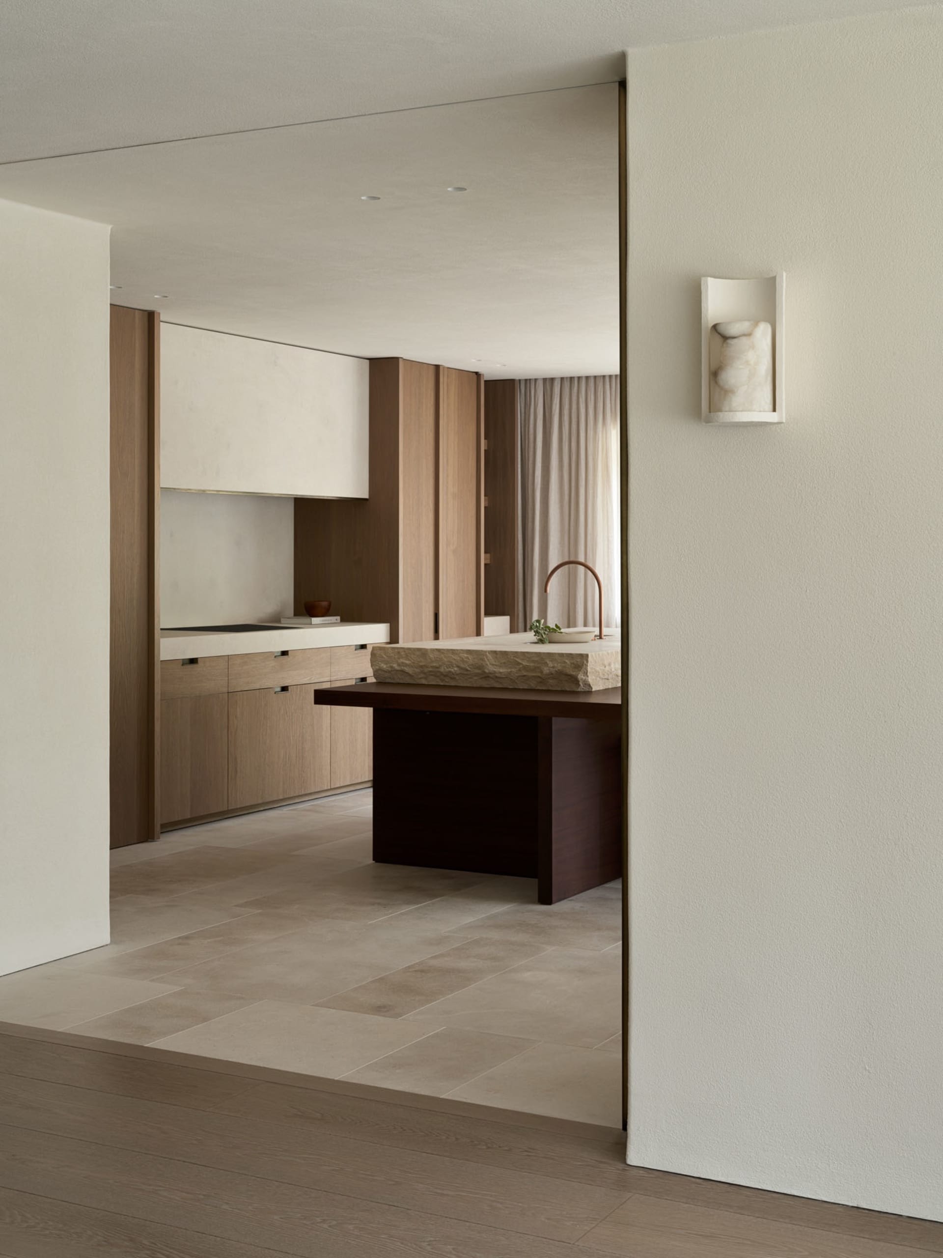 Modern kitchen with a wooden floor, white walls, a sink, dining table, and counter, with natural light from a window