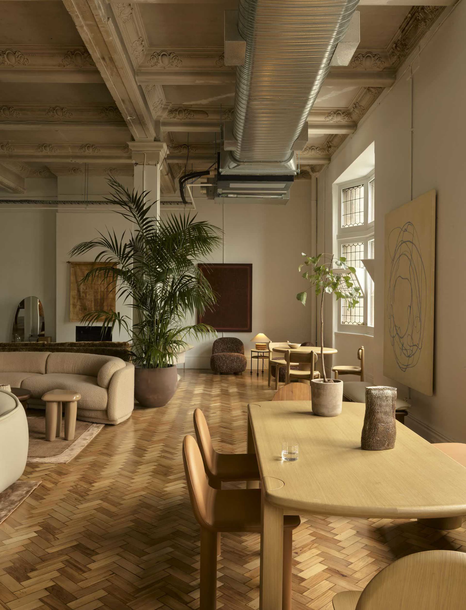 A well-lit living room with a wooden floor, a dining table, chairs, a couch, and a potted plant, creating a cozy and inviting atmosphere