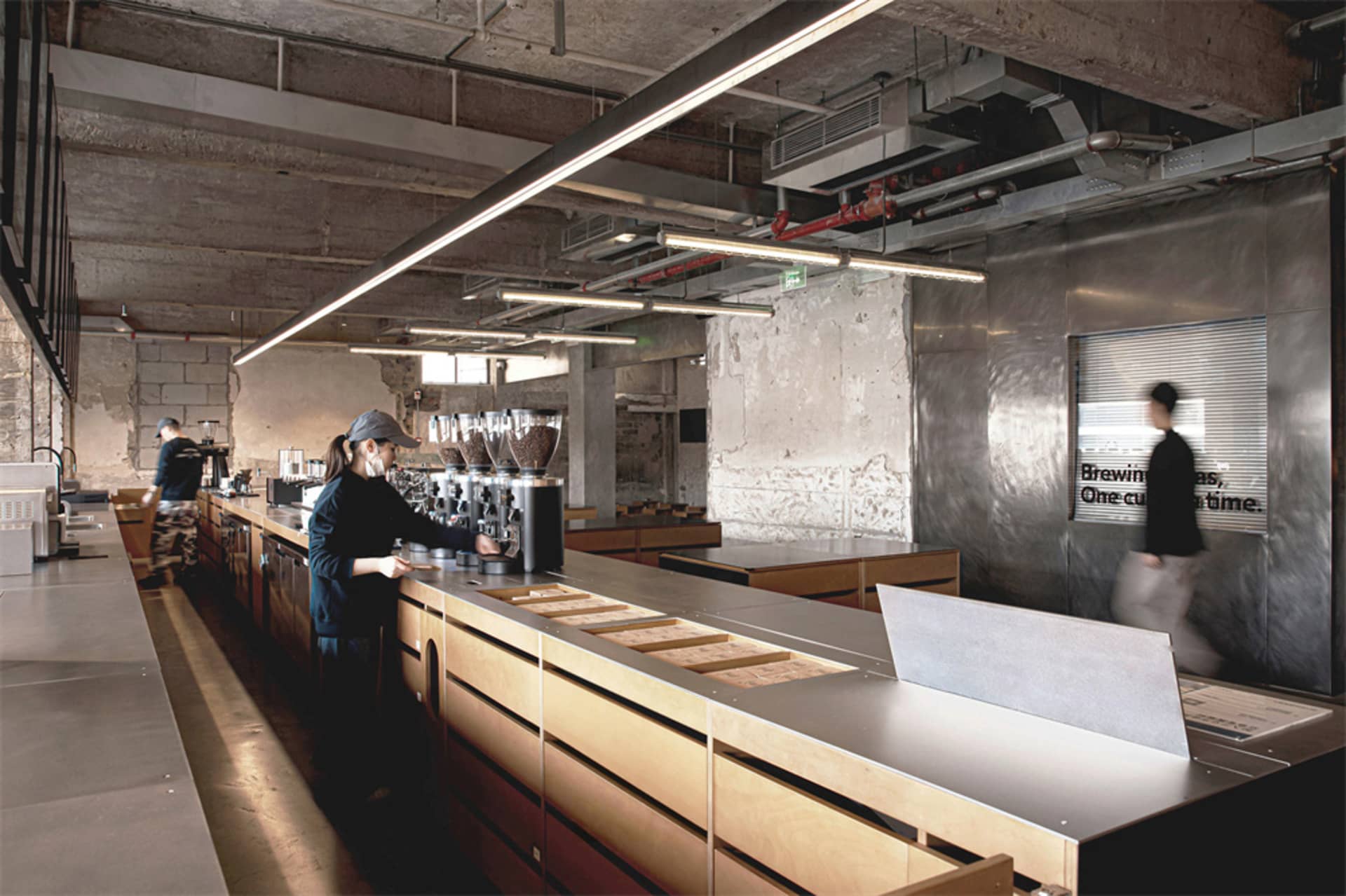 A modern coffee shop with a large counter, seating, and a warm atmosphere created by wood materials and well-lit space