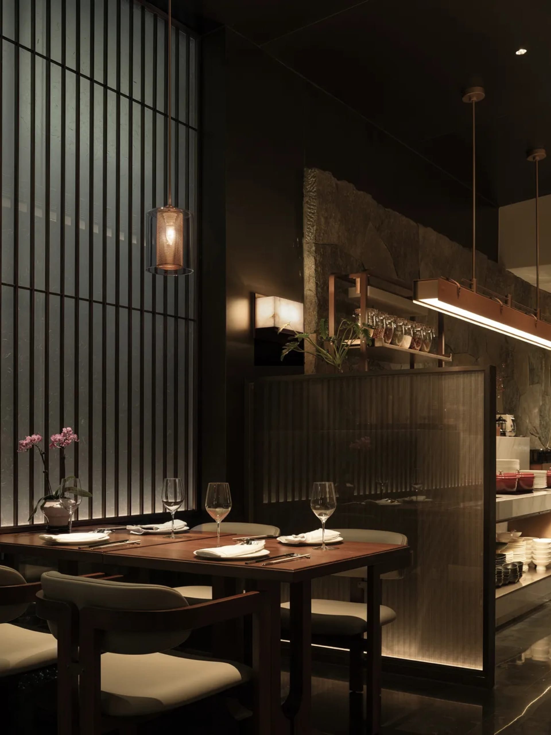 A dimly lit restaurant dining area with a table, chairs, and counter, featuring a combination of wood and metal elements, wine glasses, and decorative items