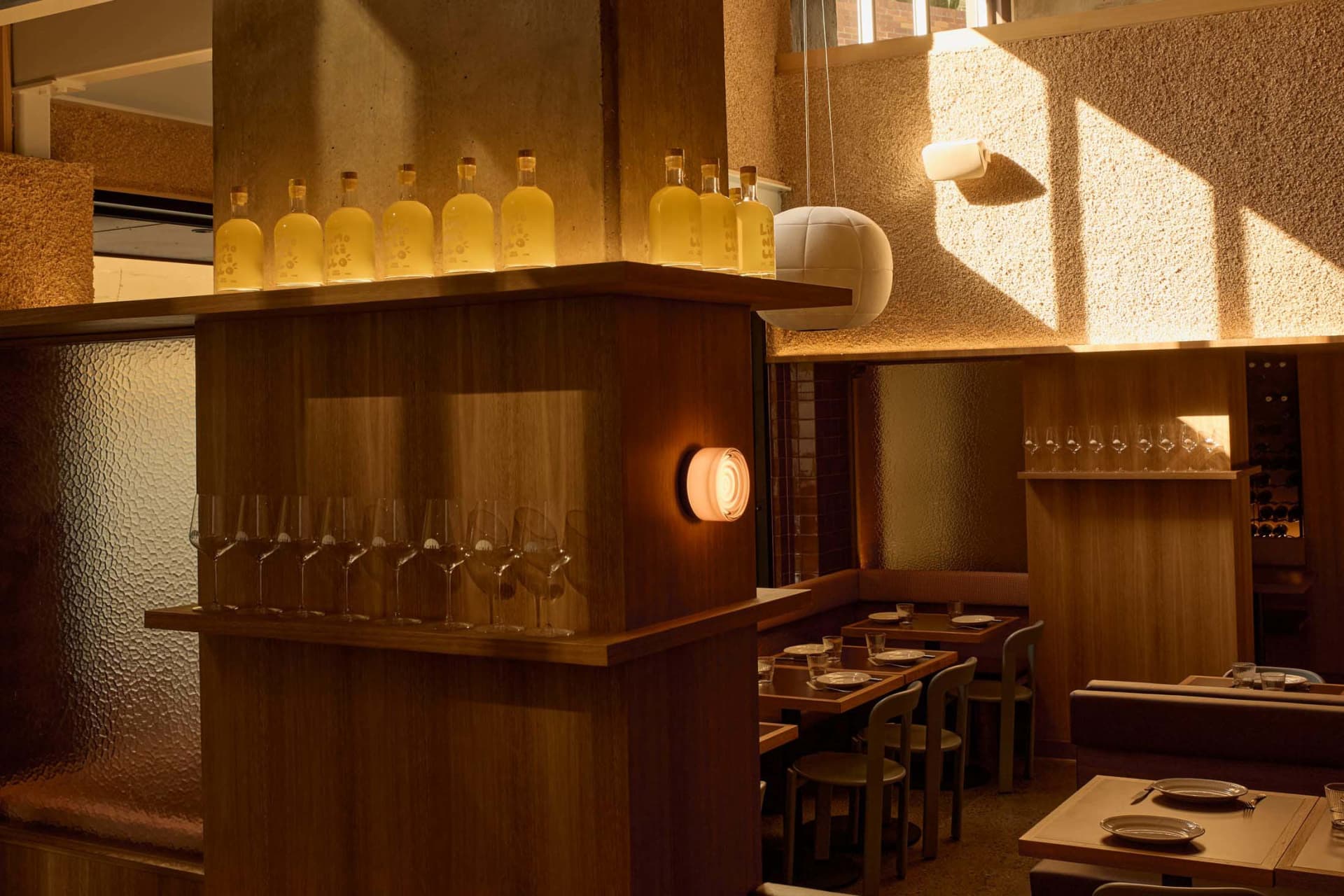 Cozy modern restaurant with a wooden bar, tables, and chairs, dim lighting, and wine glasses on tables
