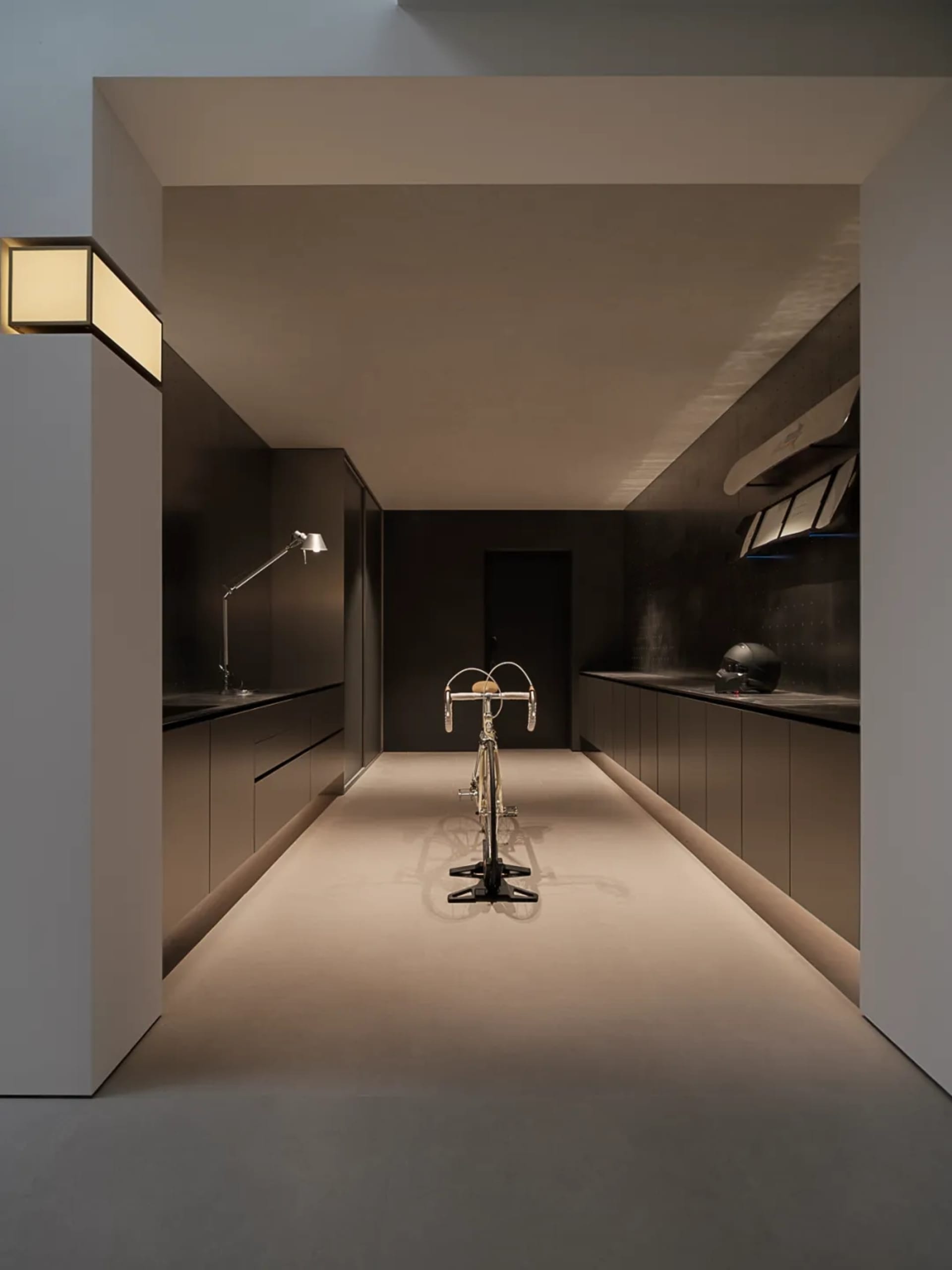 A kitchen with a bicycle parked against the wall, featuring a sink, refrigerator, and microwave, in a dimly lit space