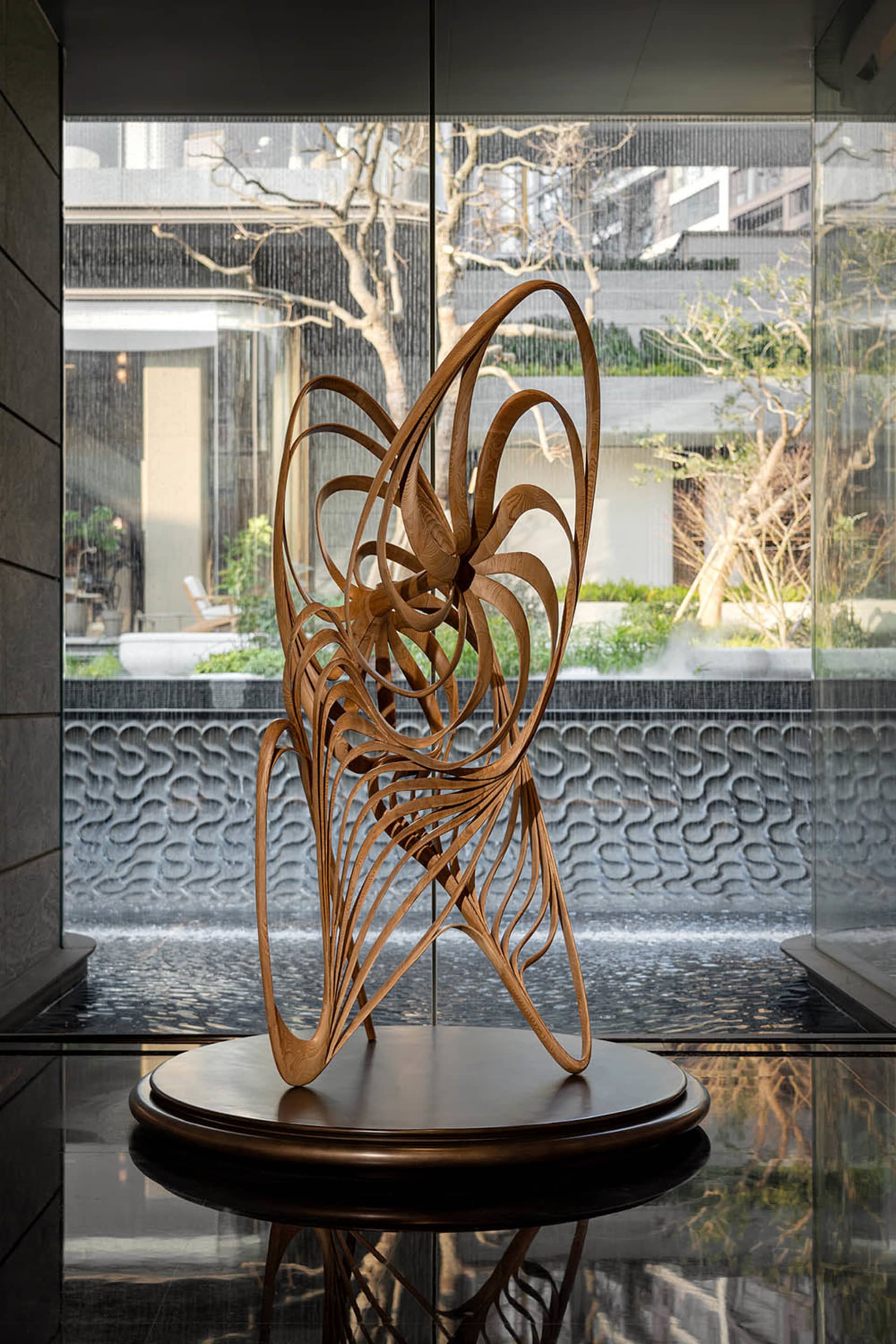 A modern room with a glass wall and a wooden sculpture in front of it, placed in a visually appealing artistic setting