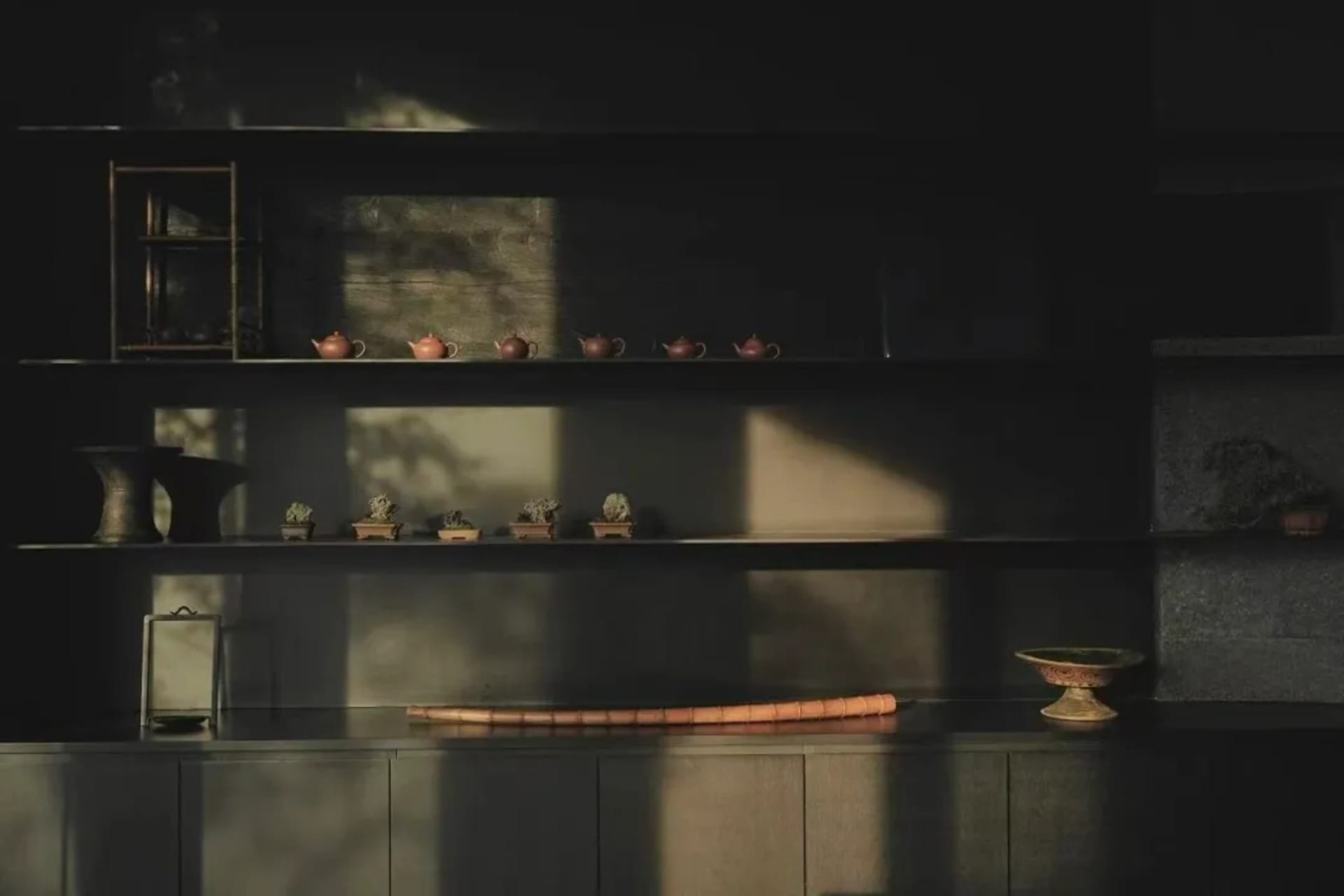 A dimly lit kitchen or dining area with a wooden shelf displaying various objects, a wooden table, and a potted plant, creating a warm and inviting atmosphere