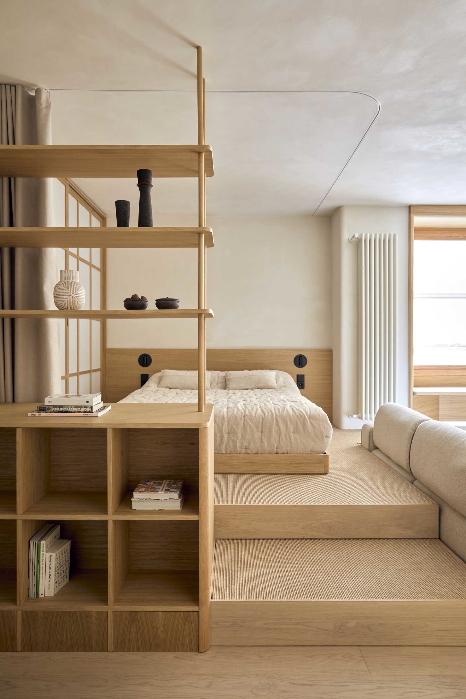 Cozy bedroom with a bed, bookshelf, and couch, featuring wood furniture and a neutral color palette