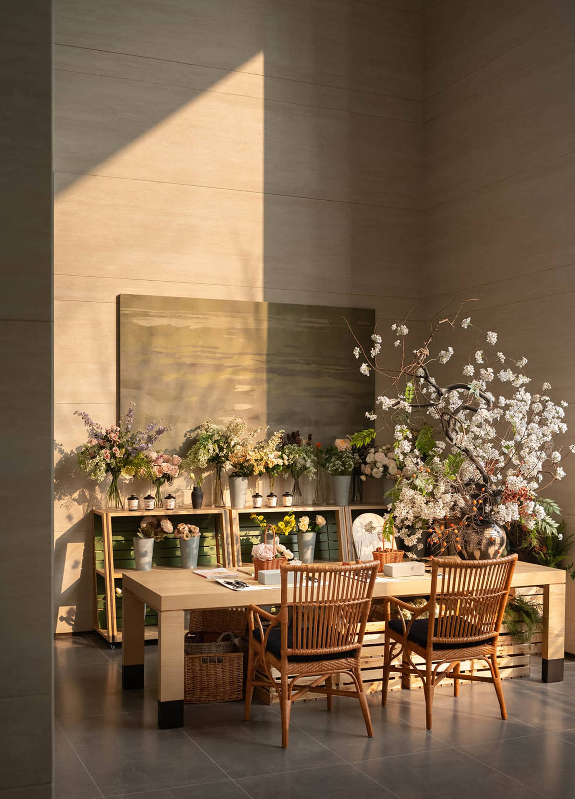A modern dining room with a wooden table, chairs, and various decorative items, surrounded by a potted plant and a vase with flowers, under soft and warm lighting