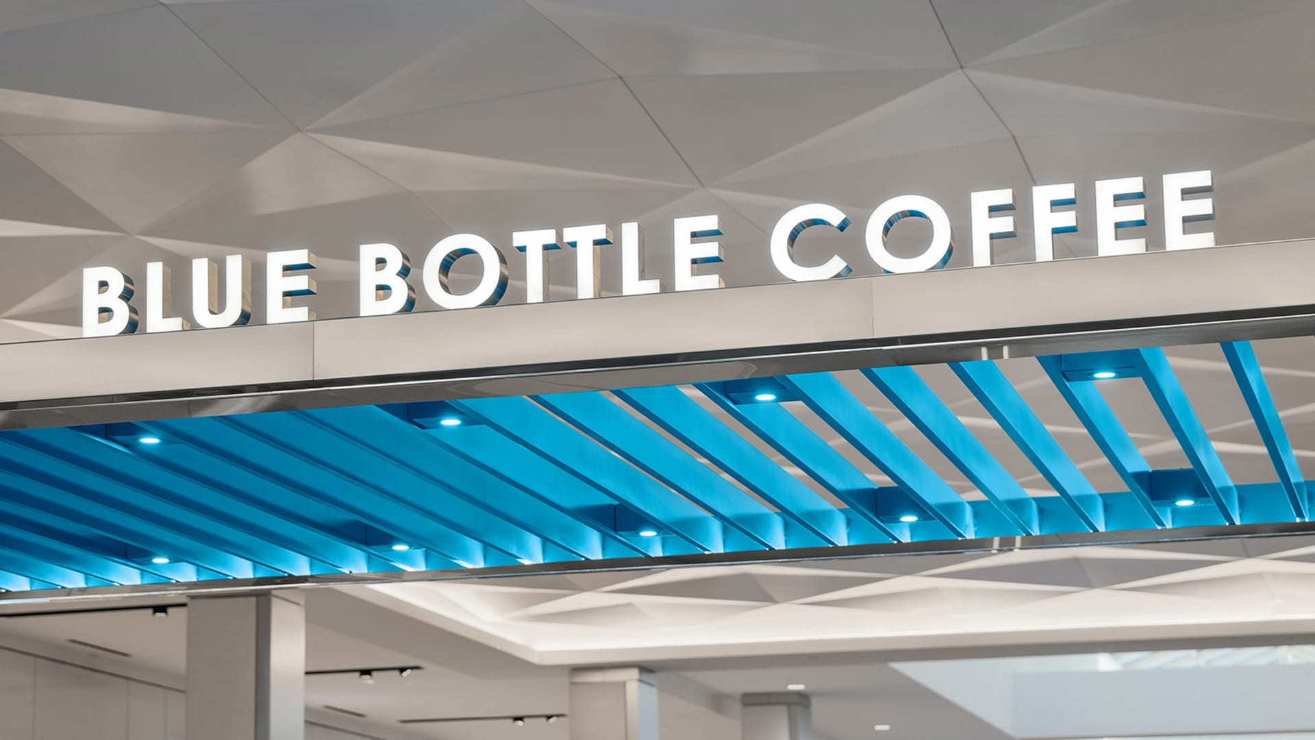 A modern coffee shop with a blue and white color scheme, featuring a large blue sign, a dining table, chairs, and a couch in a brightly lit space