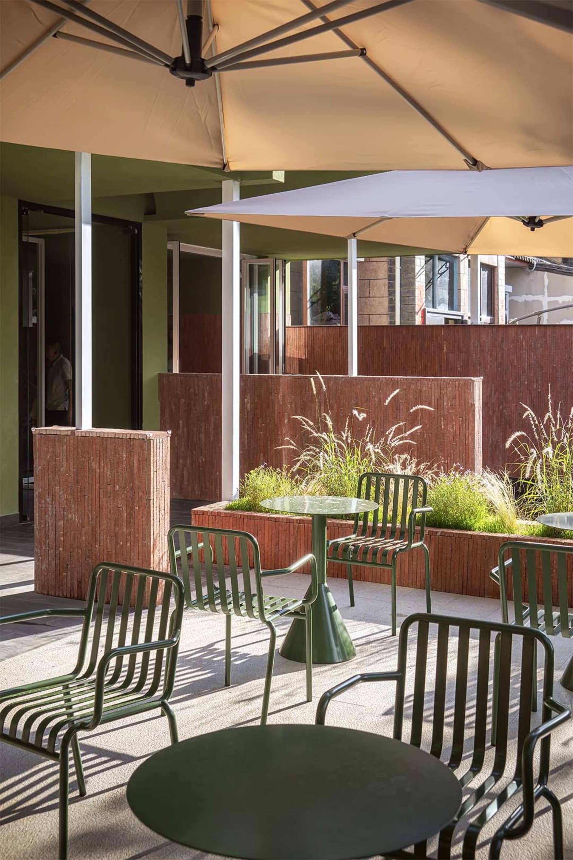 A patio dining area with a green table and chairs, shaded by a large umbrella, in a restaurant or outdoor dining setting