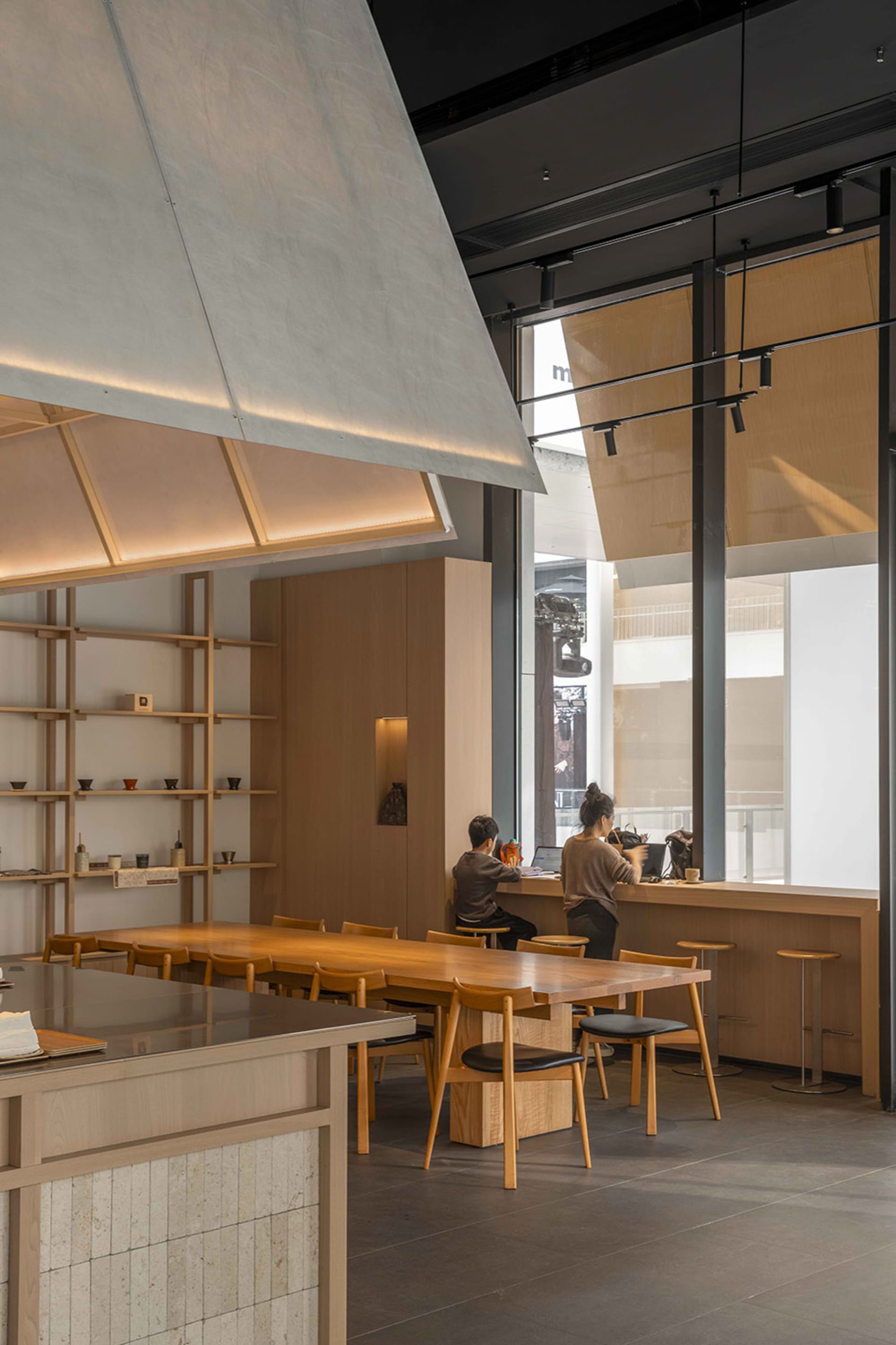 A modern restaurant interior with a dining table, chairs, counter, and kitchen elements, featuring wooden accents and a neutral color palette, with soft and warm lighting