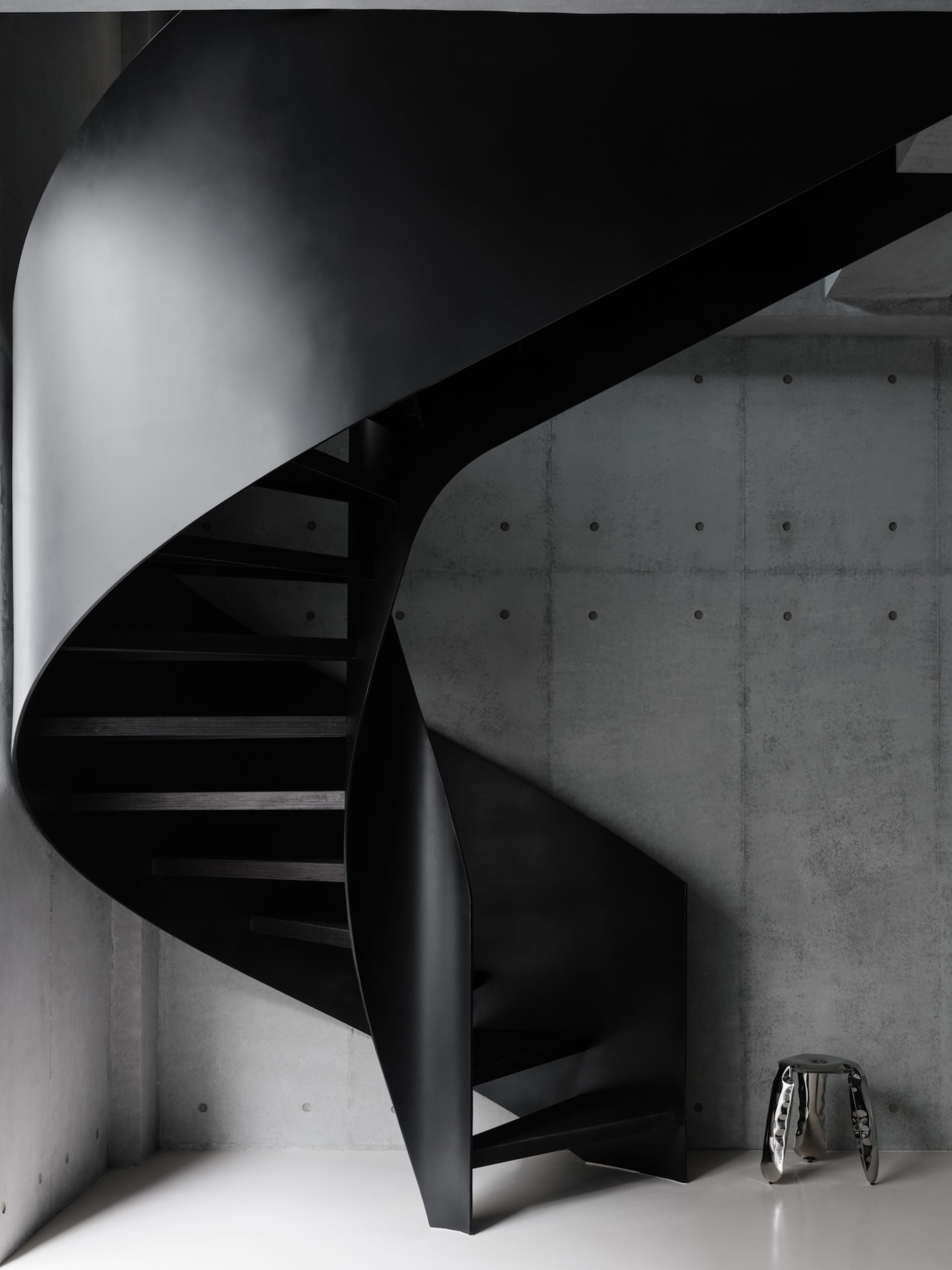 A black and white photo of a spiral metal staircase in a dimly lit room with a metal trash can at the base