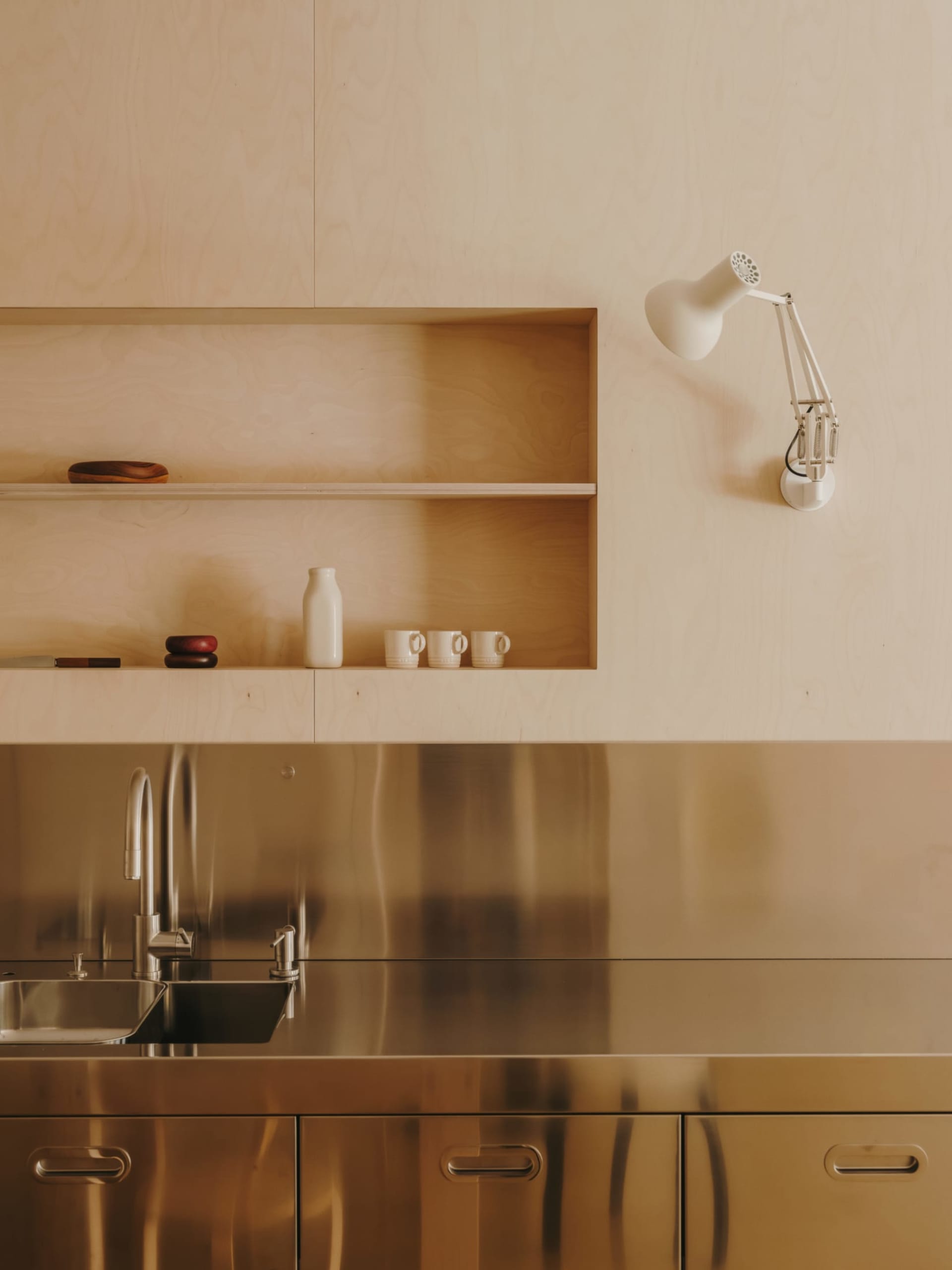 Residential kitchen with a metal sink and wooden shelf, featuring modern style and natural lighting